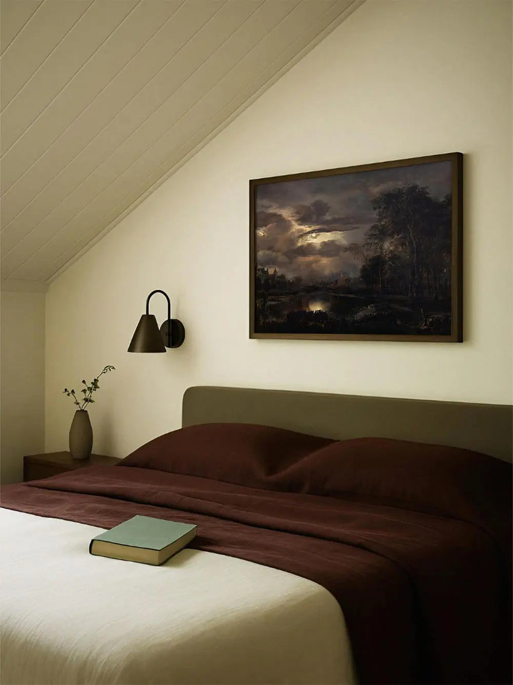 Der Landschafts-Kunstdruck mit Mondschein hängt über einem Bett mit dunkler Decke. Die stille Nachtstimmung unterstreicht die behagliche Einrichtung.