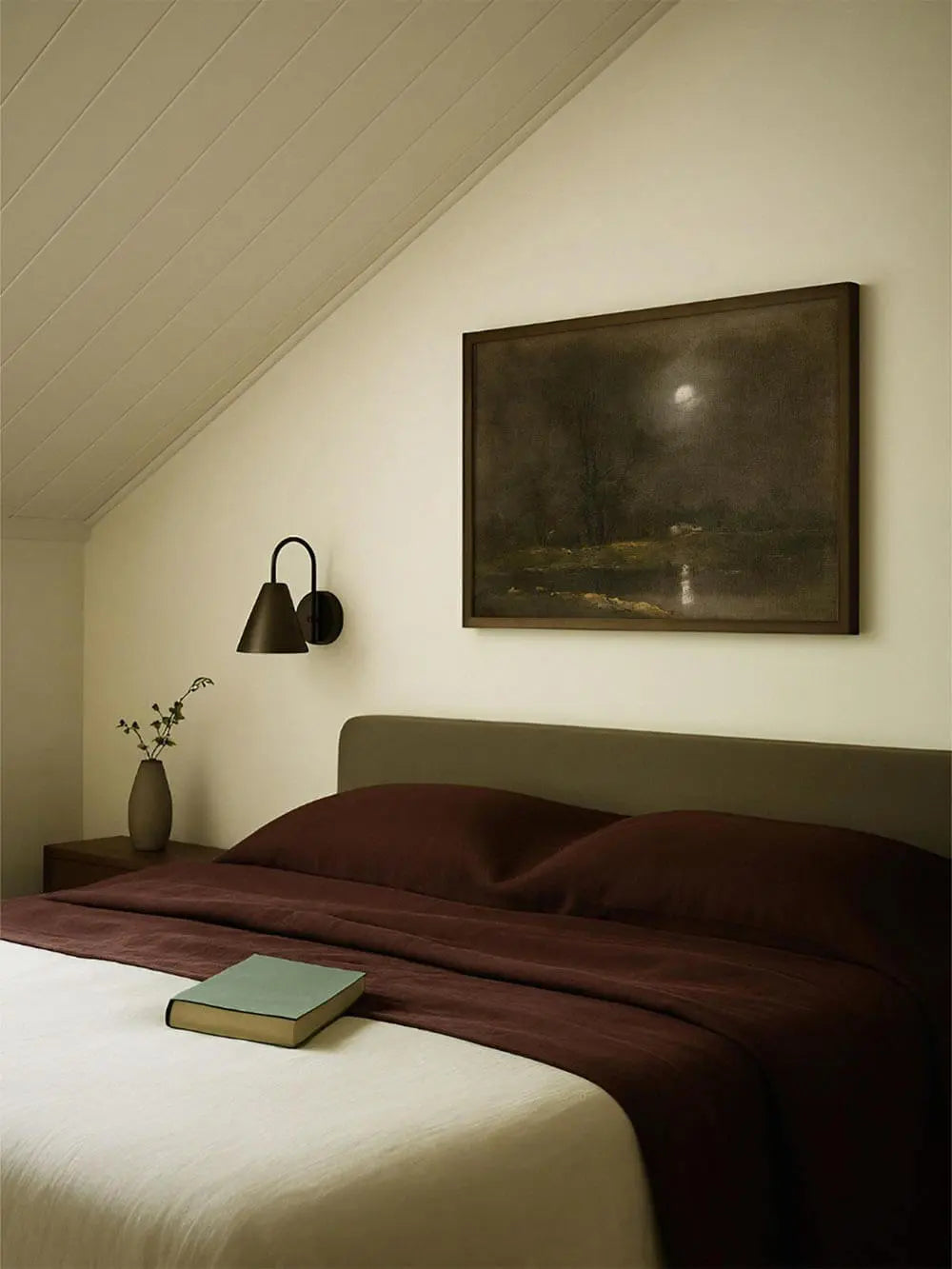 Dunkler Landschafts-Kunstdruck mit Mondschein hängt gerahmt über einem Bett. Das Vintage Wandbild schafft eine ruhige, nostalgische Stimmung im Schlafzimmer.