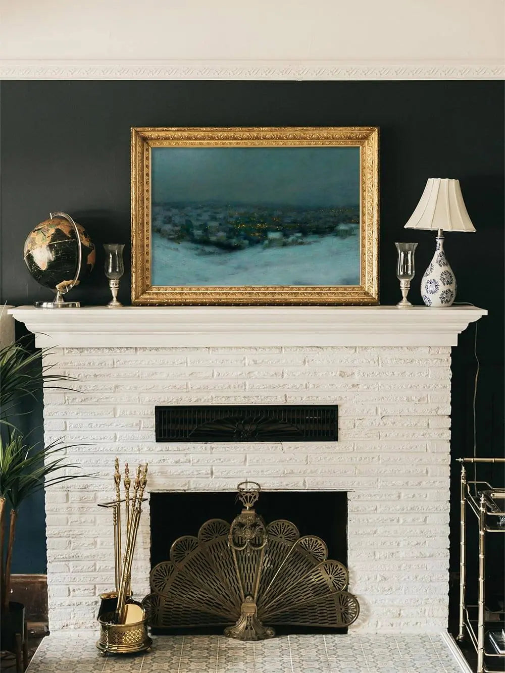 Gerahmter Winterlandschaft Kunstdruck über einem Kamin mit dunkler Wand, das Zusammenspiel aus kühlen Farben und warmem Goldrahmen schafft einen edlen Vintage-Akzent.