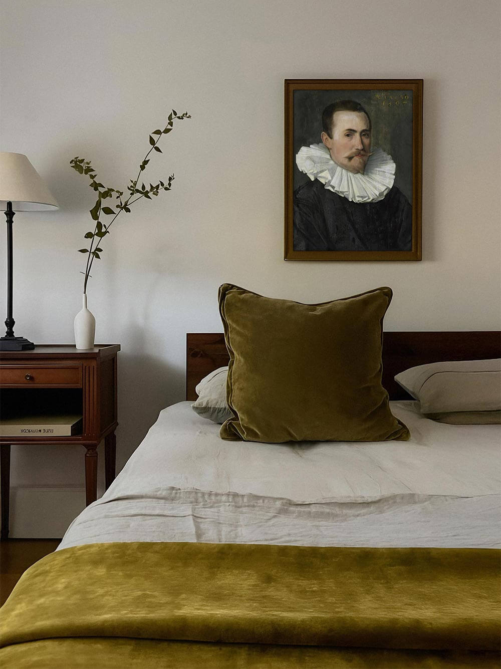 Vintage Wandbild eines Renaissance-Herren über dem Bett mit samtgrünen Akzenten. Der Kunstdruck fügt sich harmonisch in das minimalistische Interieur mit klassischer Note.