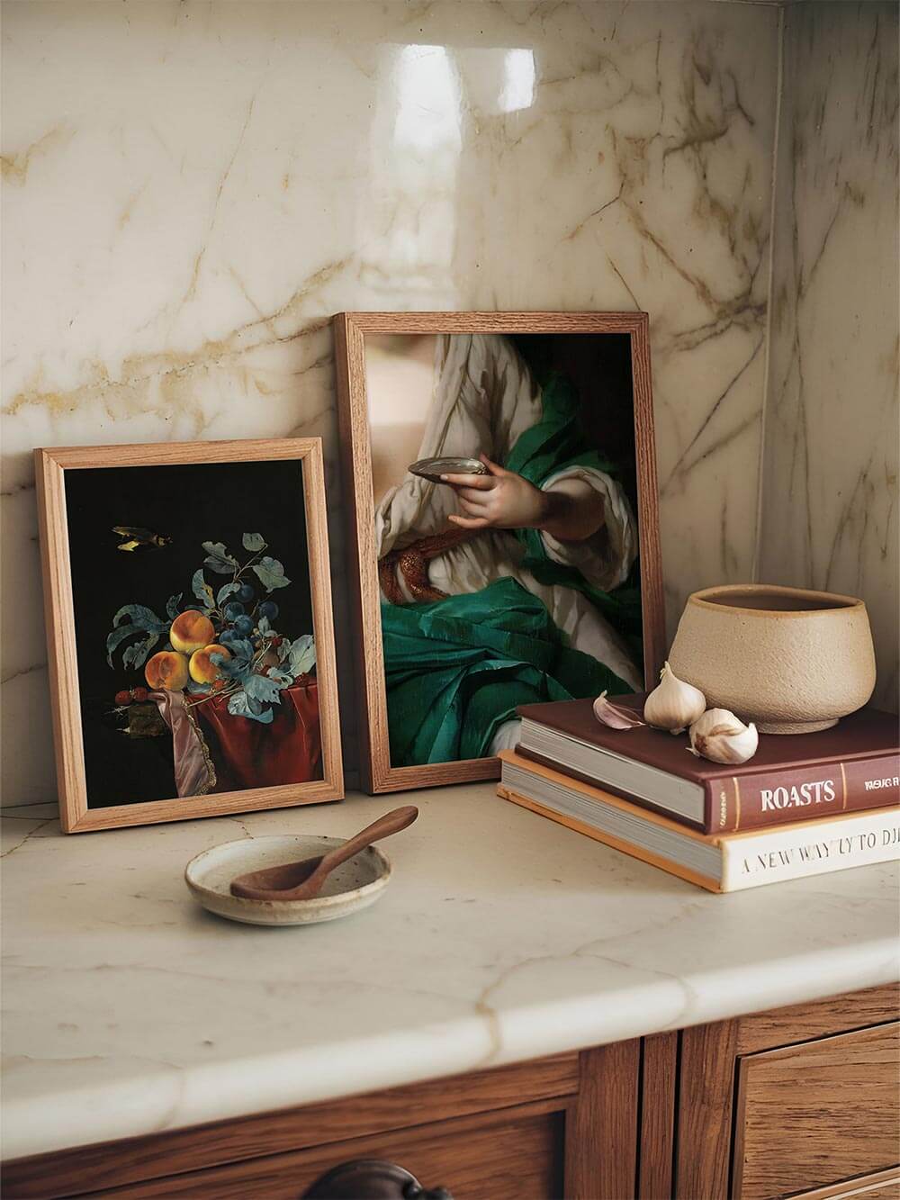 Zwei gerahmte barocke Kunstdrucke auf einer Marmorarbeitsfläche mit Büchern und Knoblauchdeko. Harmonisches Stillleben mit historischen Akzenten, perfekt für Küche oder Essbereich im Vintage-Stil.