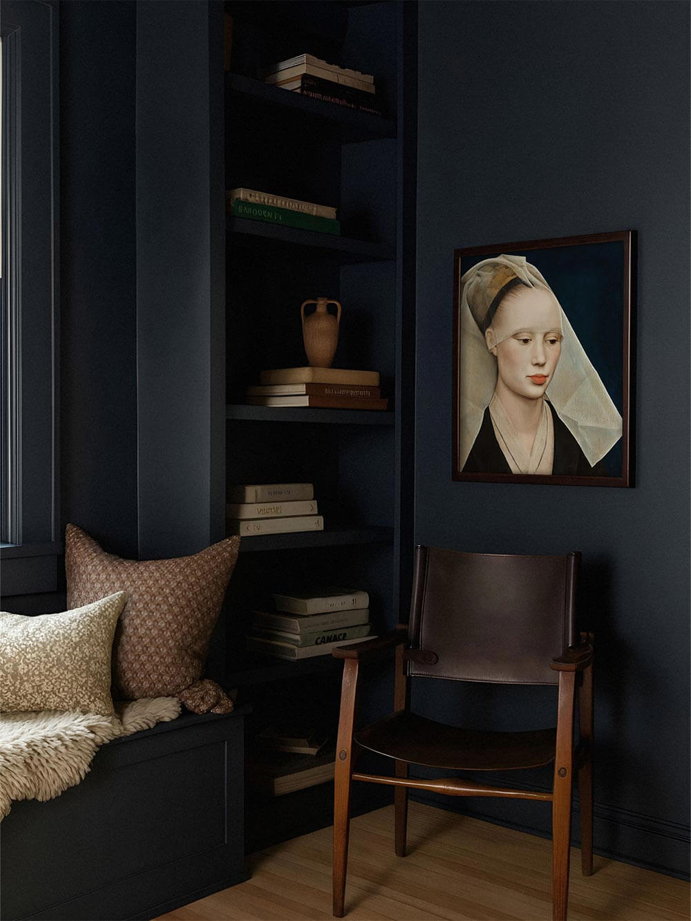 Gerahmtes Porträt einer Frau im Schleier hängt an einer dunkelblauen Wand neben Regal und Ledersessel. Moody Interieur kombiniert mit klassischer Kunst für eine elegante, ruhige Raumwirkung.