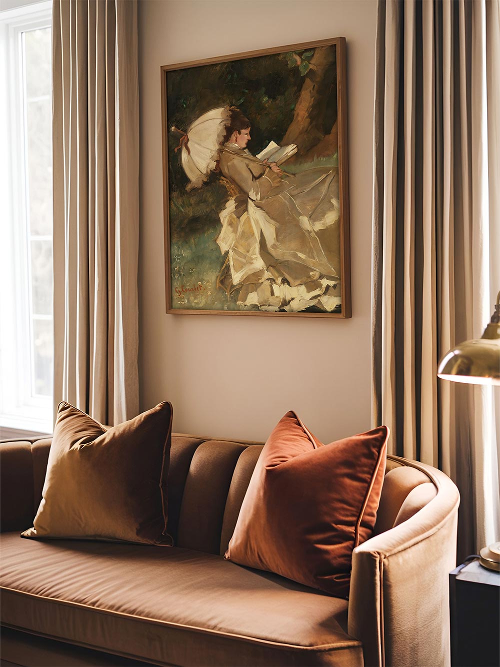 Gerahmtes Wandbild mit klassischem Lesemotiv über beigem Sofa zwischen Vorhängen und Fensterlicht, kombiniert mit Kissen als harmonisches Highlight für elegante Wohnräume und stilvolle Galerie-Wände.