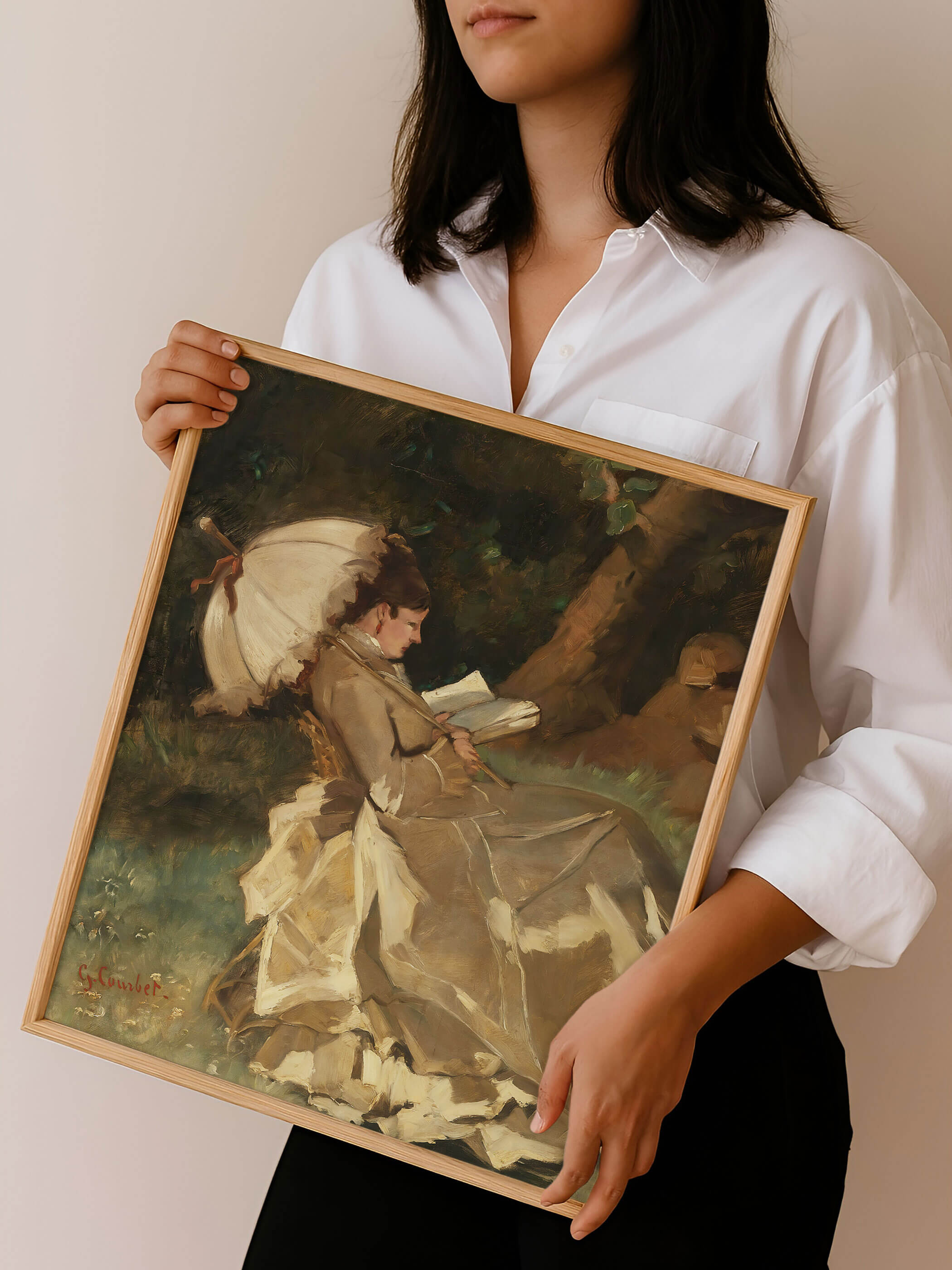 Person hält den gerahmten Kunstdruck mit lesender Frau vor neutralem Hintergrund, zeigt Format und Proportionen des Posters im Verhältnis zum Körper, geeignet zur Orientierung für Wandgestaltung im Wohn- oder Arbeitszimmer.