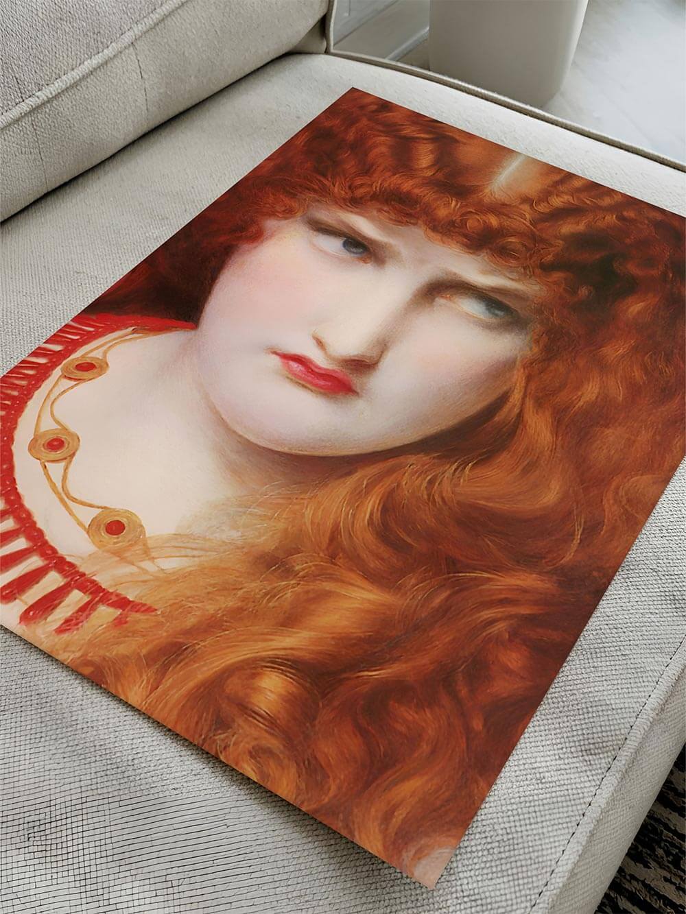 Der Porträt-Kunstdruck liegt ungerahmt auf einem beigen Sofa, die roten Locken und das leuchtende Dekolleté prägen das Bild. Der Print wirkt plastisch und farbintensiv.