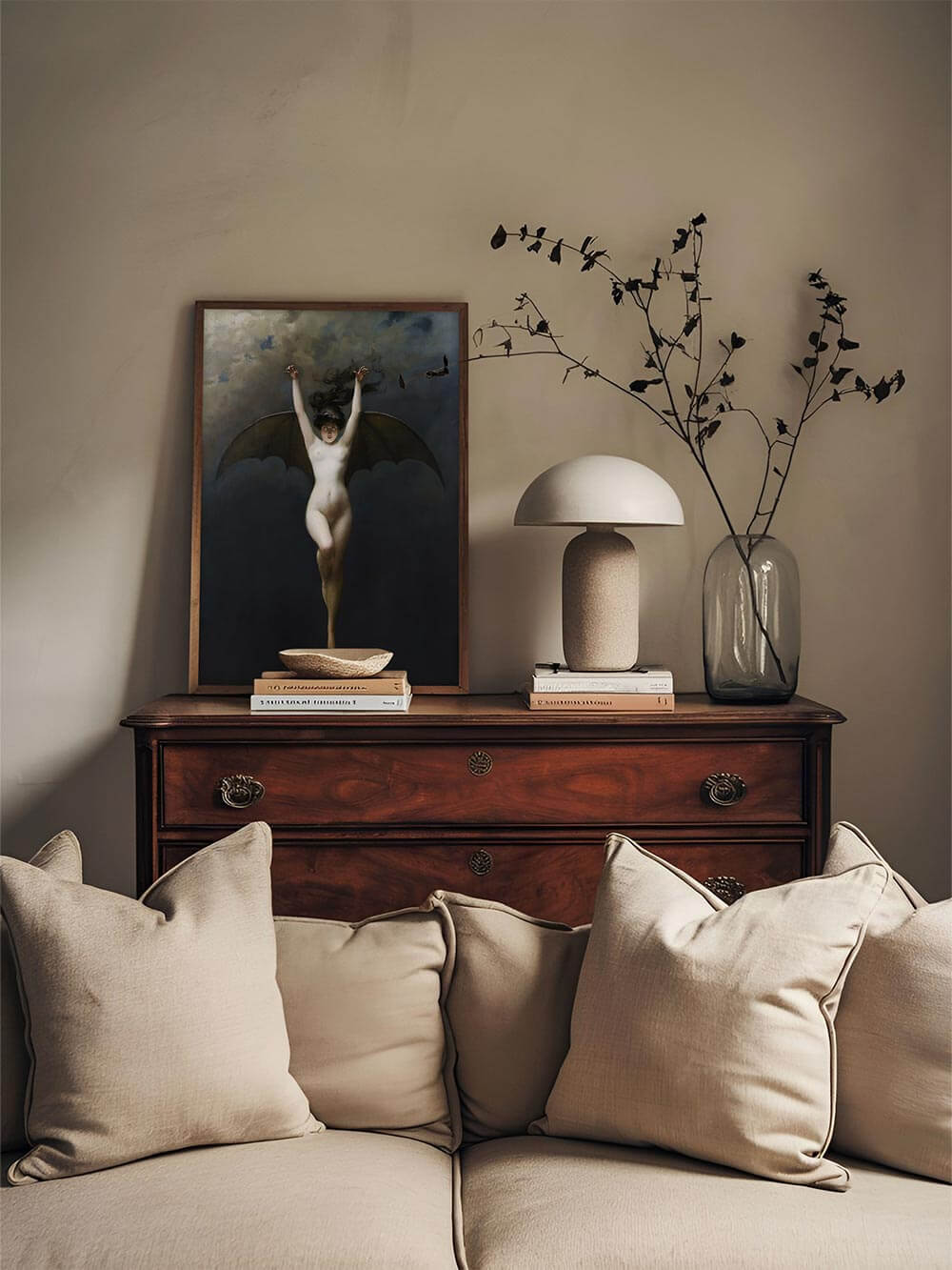 Ein Dark-Academia-Kunstdruck mit einer geflügelten Frau, gerahmt auf einem antiken Holzsideboard, dekoriert mit minimalistischer Keramik und Ästen – der mystische Charakter des Bildes wirkt als stilvoller Eyecatcher im Wohnraum.