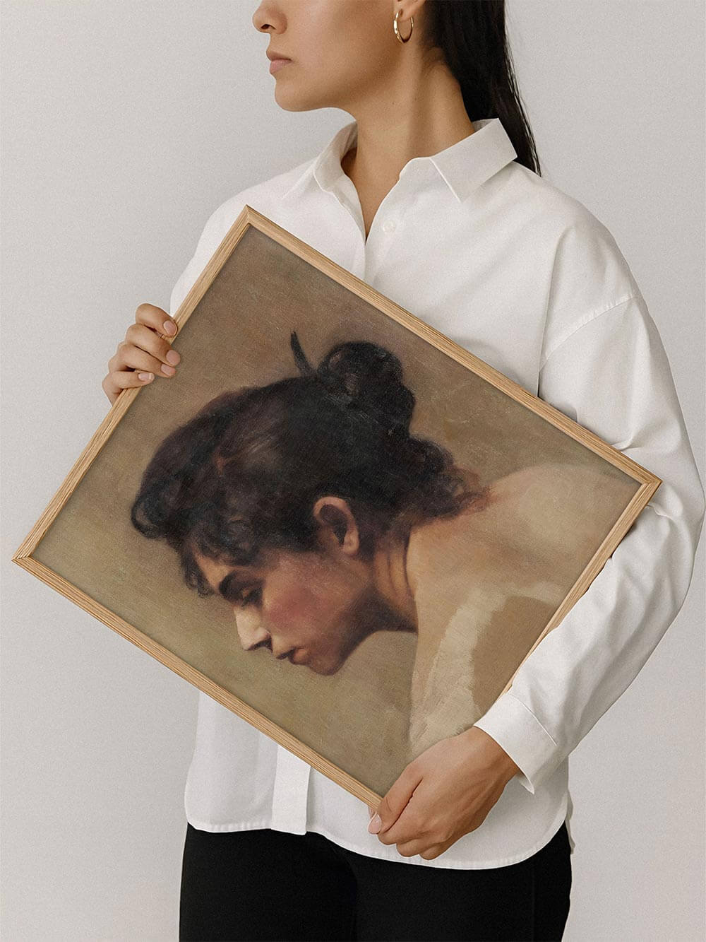 Eine Frau hält den gerahmten Kunstdruck mit dem Seitenprofil eines Frauenportraits. Das warme Vintage Wandbild strahlt Ruhe aus und eignet sich als zeitloses Kunstwerk für jedes Zuhause.