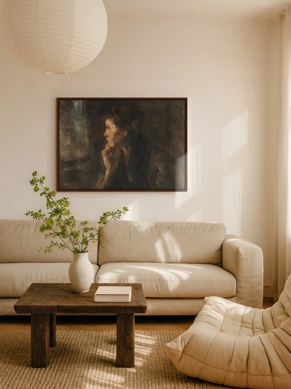 Dunkles Leinwandbild mit Frauenprofil im braunen Rahmen über einem beigen Leinensofa, davor ein Couchtisch aus altem Holz mit Vase und grünen Zweigen