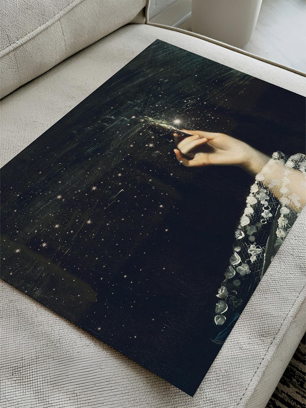 Quadratischer Kunstdruck liegt auf einem hellen Stoffsofa und zeigt die leuchtende Hand vor tiefdunklem, schimmerndem Hintergrund. Modernes Flatlay zur Darstellung von Format und Farbwirkung, geeignet für Galerie-Wand oder stilvolle Wohnräume.