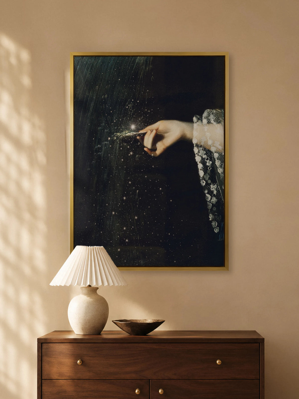 Dunkles Leinwandbild mit Sternenregen im goldenen Rahmen über einer Kommode aus Nussbaum mit Plisseeleuchte und Schale aus Bronze im Abendlicht