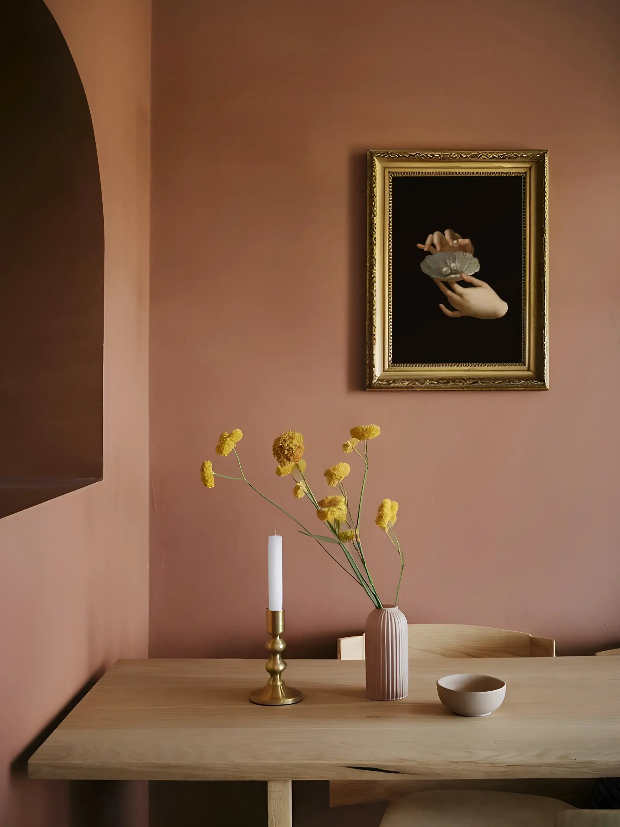Barock Kunstdruck mit Händen und Perlenmuschel in goldenem Zierrahmen hängt an einer terrakottafarbenen Wand über einem Holztisch mit Kerzenständer. Das kontrastreiche Wandbild passt zu einem warmen, mediterranen Esszimmerstil.