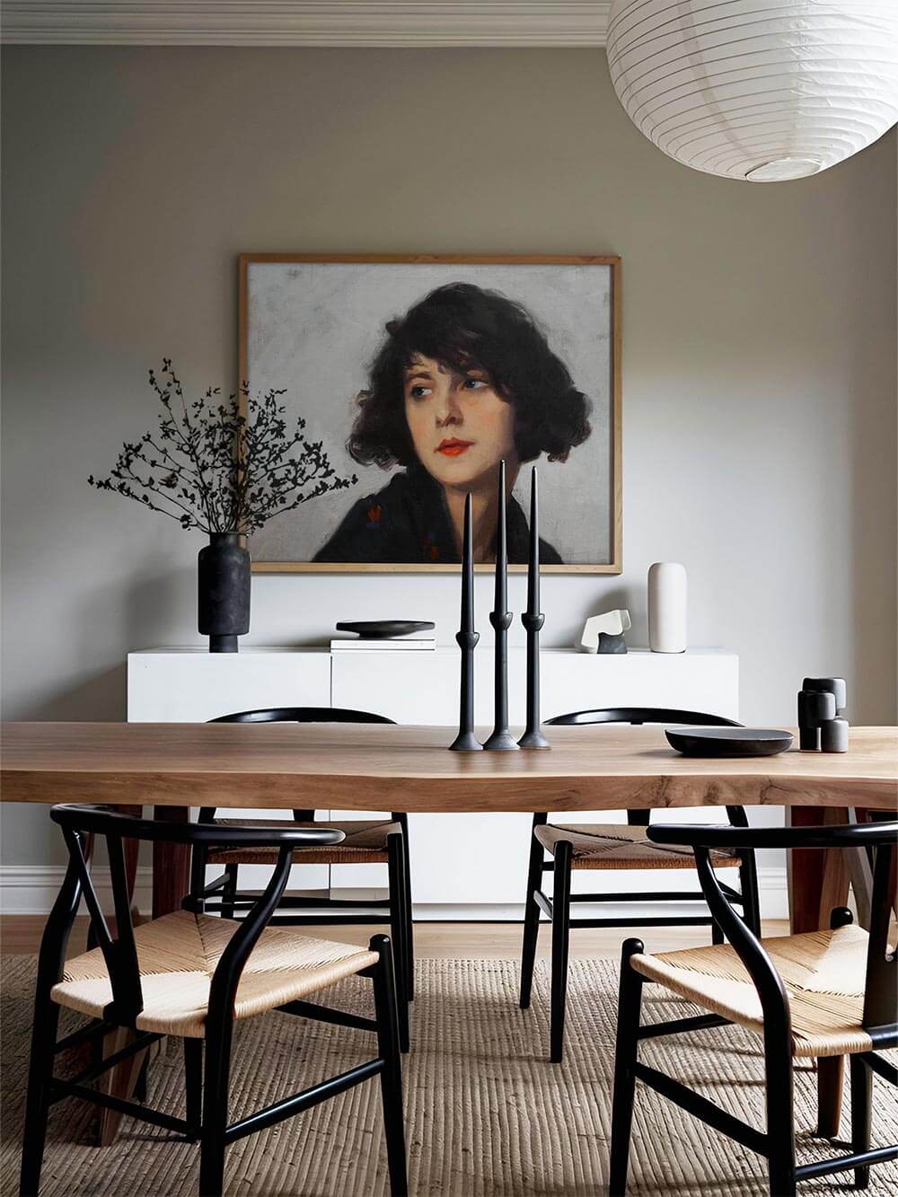 Porträt einer nachdenklich blickenden Frau mit schwarzem Haar und rotem Mund, als gerahmter Kunstdruck über einem Sideboard im skandinavischen Esszimmer mit klaren Linien und warmem Holz.