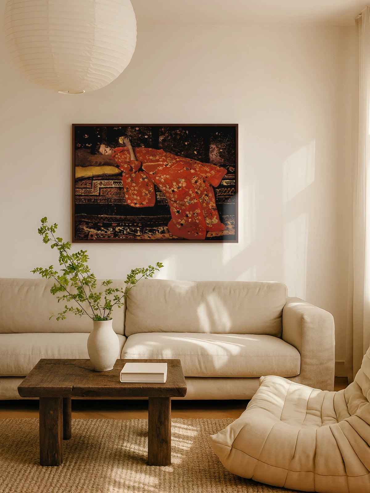 Das Moody Leinwandbild mit Mädchen im roten Kimono hängt im braunen Rahmen über einem beigen Leinensofa im Wohnzimmer. Davor steht ein rustikaler Couchtisch aus dunklem Holz mit einer weißen Vase voller grüner Zweige, darüber eine Papierlampe.