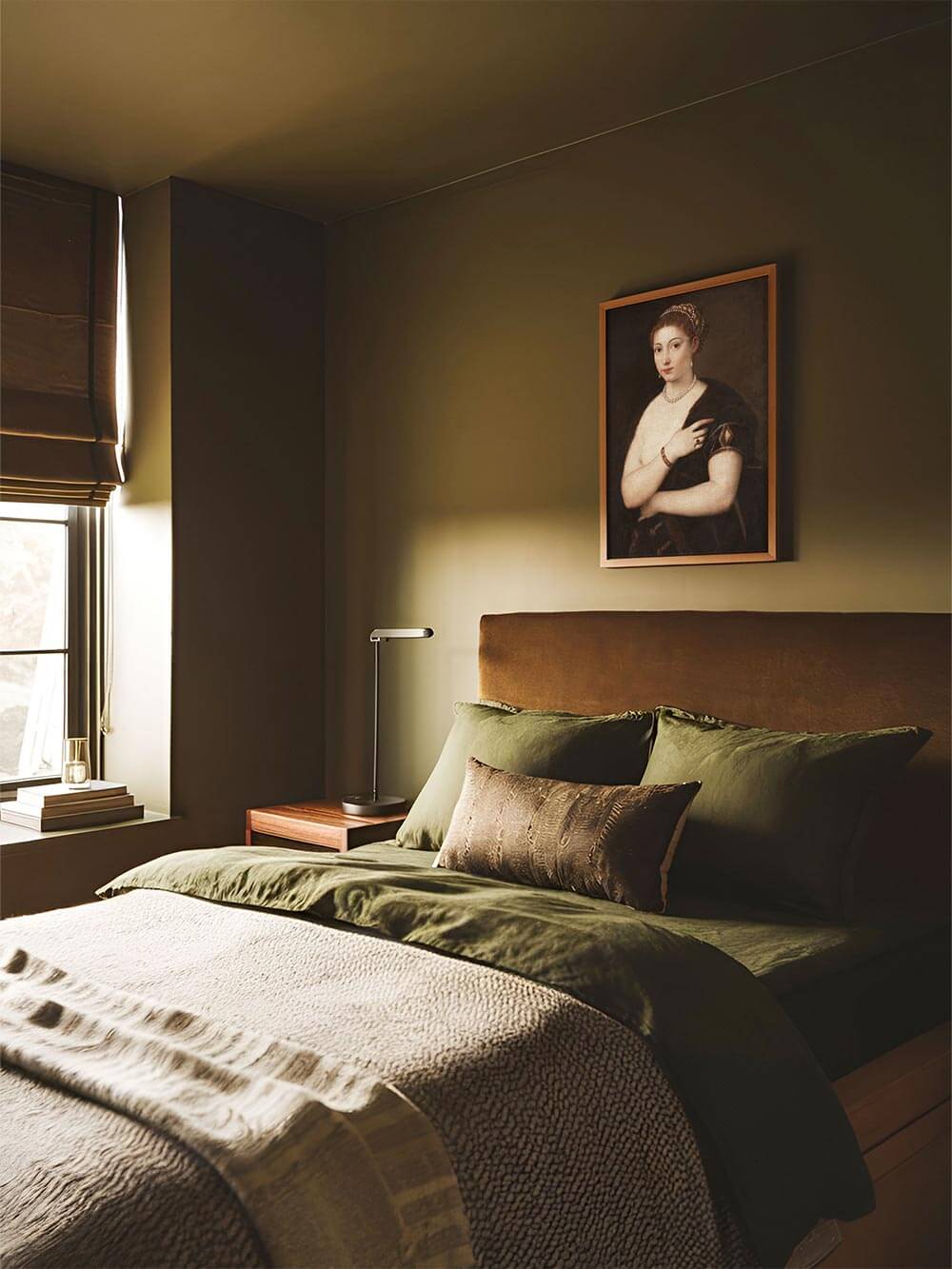 Renaissance-Kunstdruck einer Frau mit Perlenkette hängt über einem olivgrünen Bett in sanft beleuchtetem Raum. Harmonische Kombination aus klassischer Kunst und moody Interior-Stil.