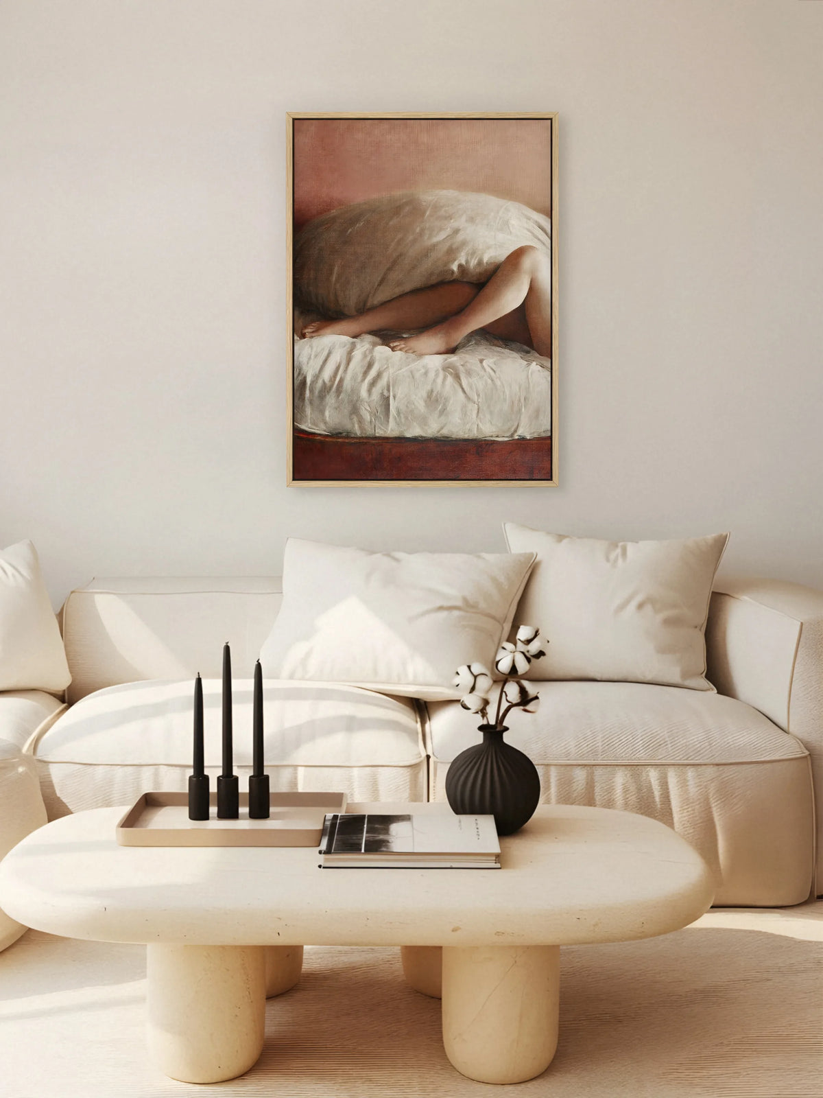Akt Leinwandbild in Rosé und Creme im naturfarbenen Rahmen über einem cremefarbenen Sofa, davor ein runder Couchtisch mit schwarzen Kerzen