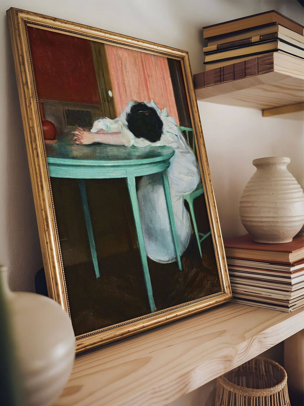 Vintage-Kunstdruck einer erschöpften Frau mit dem Kopf auf einem grünen Tisch, in einem goldfarbenen Rahmen, der dekorativ auf einem Holzregal zwischen Büchern und einer Keramikvase steht.
