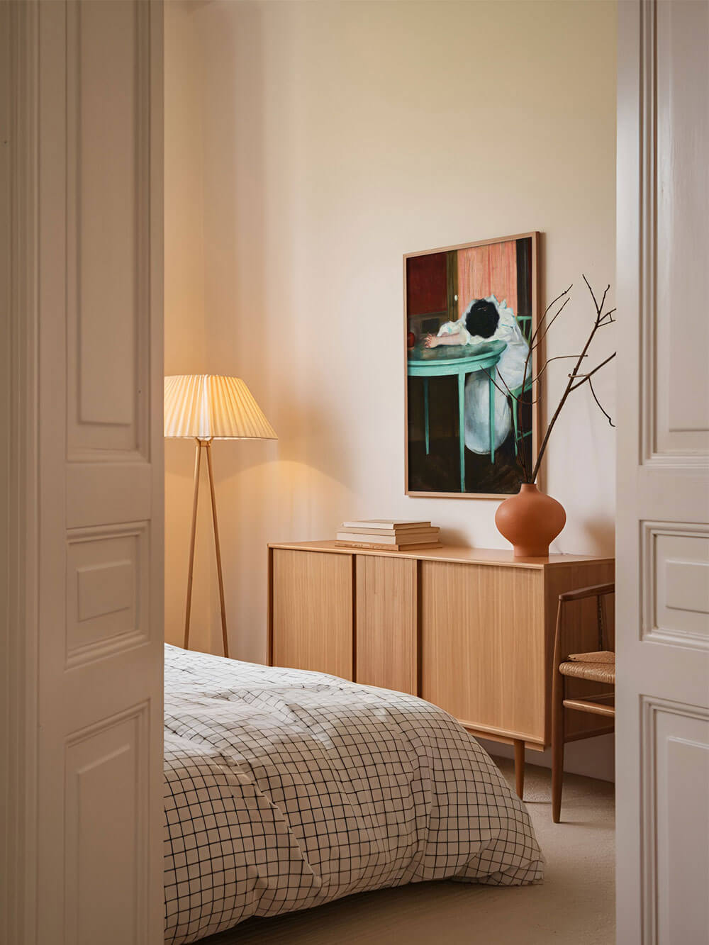 Vintage-Kunstdruck einer Frau, die erschöpft am Tisch sitzt, in einem modernen Schlafzimmer an einer hellen Wand neben einer Stehlampe und über einer Holzkommode platziert."