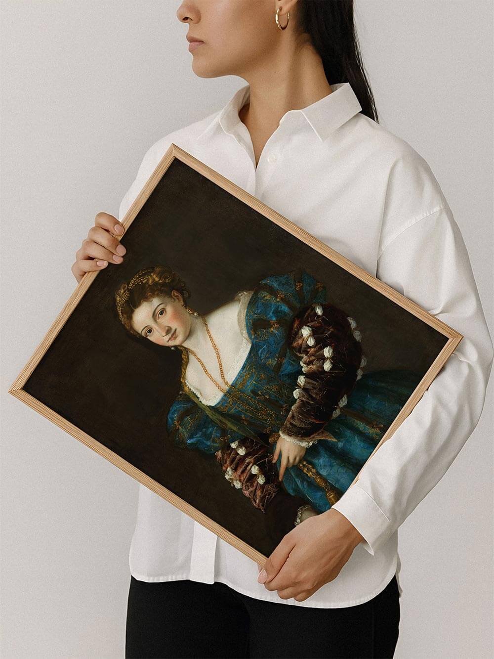 Frau hält gerahmten Renaissance-Kunstdruck mit feinen Stoff- und Schmuckdetails. Zeitloses Porträt als dekoratives Wandbild für kunstvolle Wohnräume und stilvolle Galerie-Wände.