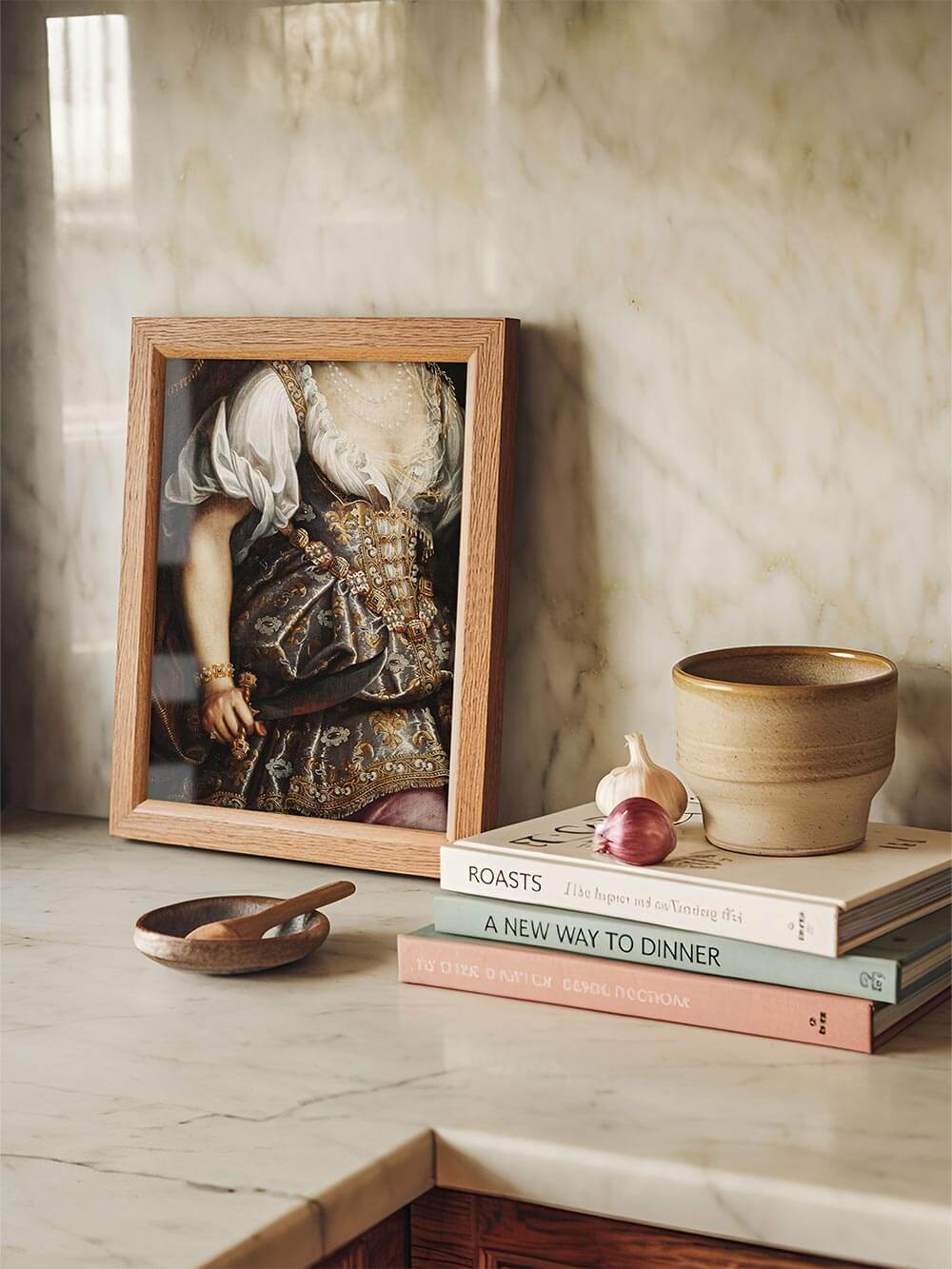 Ein gerahmter Kunstdruck mit einem barocken Porträt, das eine reich verzierte Robe mit goldenen Stickereien und Schmuck zeigt, elegant auf einer Marmor-Küchenplatte neben Büchern und Keramikgefäßen dekoriert.
