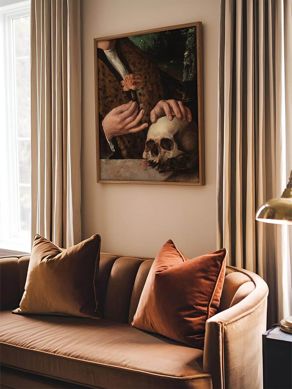 Vanitas-Wandbild über einem Samtsofa in warmen Brauntönen. Das barocke Stillleben mit Schädel und Blume schafft eine stimmungsvolle, nachdenkliche Atmosphäre in moody oder Dark-Academia-Wohnräumen.