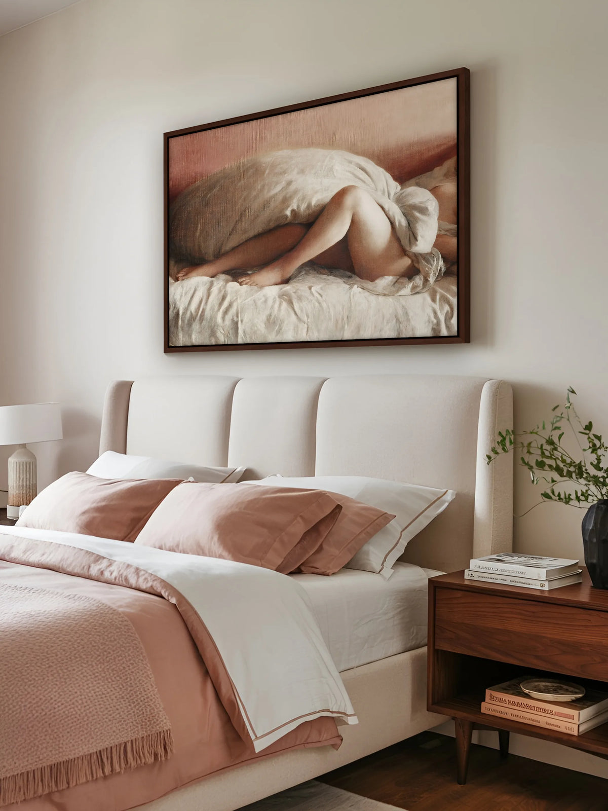 Aktgemälde auf Leinwand im braunen Rahmen über einem Polsterbett in Creme mit rosé und weißer Bettwäsche. Daneben steht ein Nachttisch aus Nussbaum mit Büchern und einer schwarzen Vase mit grünen Zweigen.