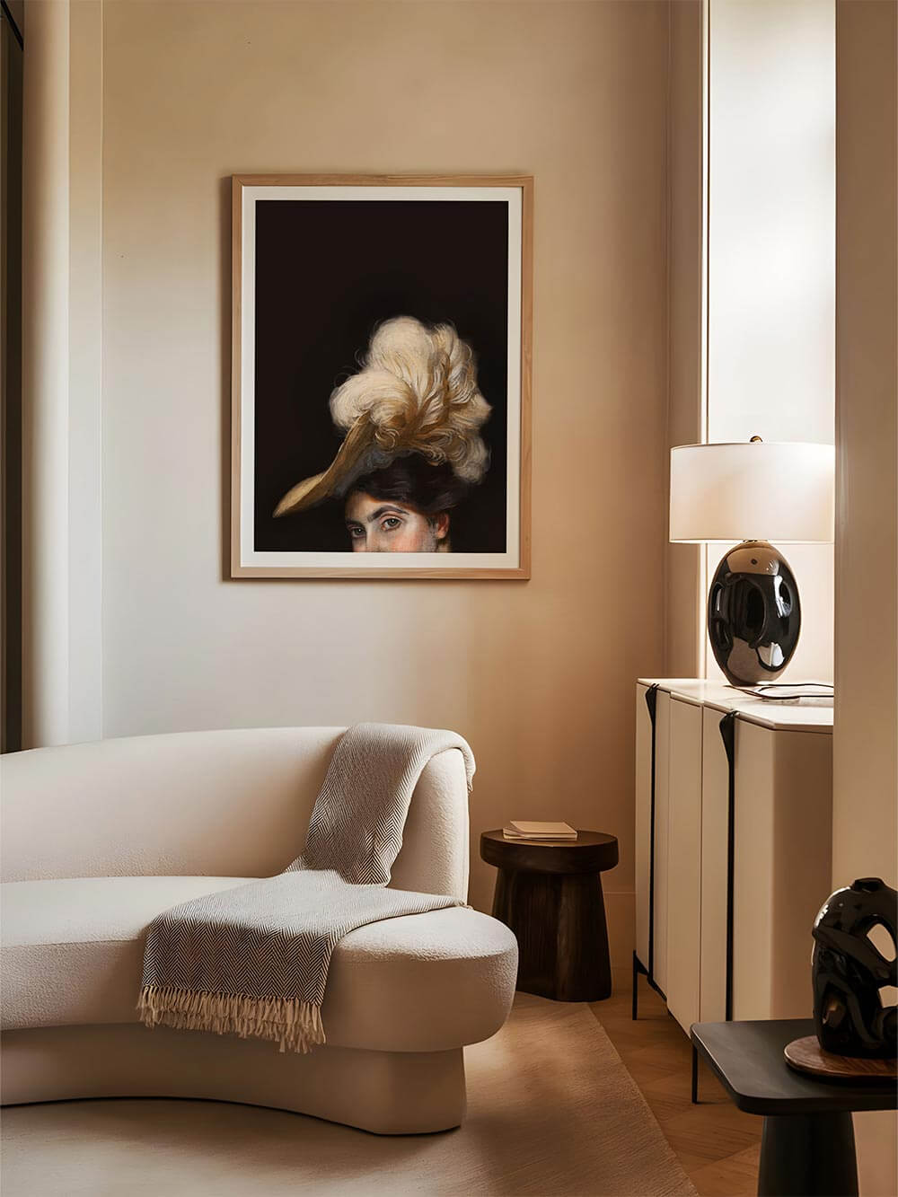 Klassisches Frauenporträt im Vintage-Stil mit Federhut als Kunstdruck in Holzrahmen, aufgehängt über einem gebogenen Sofa. Dunkler Hintergrund kontrastiert mit warmer Raumgestaltung.