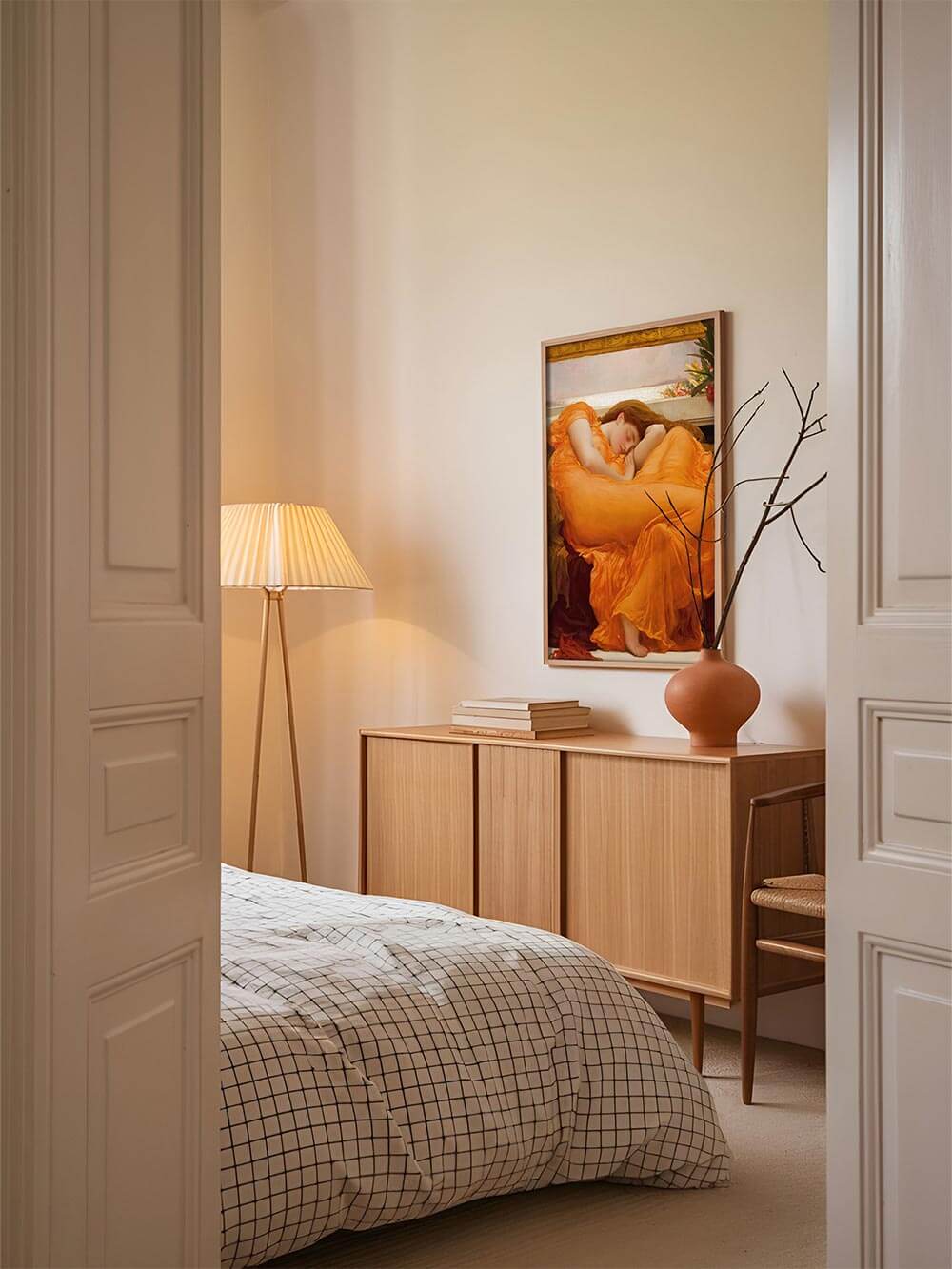 Romantischer Kunstdruck einer schlafenden Frau in leuchtendem Orange, stilvoll inszeniert über einer Kommode im Schlafzimmer mit warmem Licht und minimalistischer Einrichtung.
