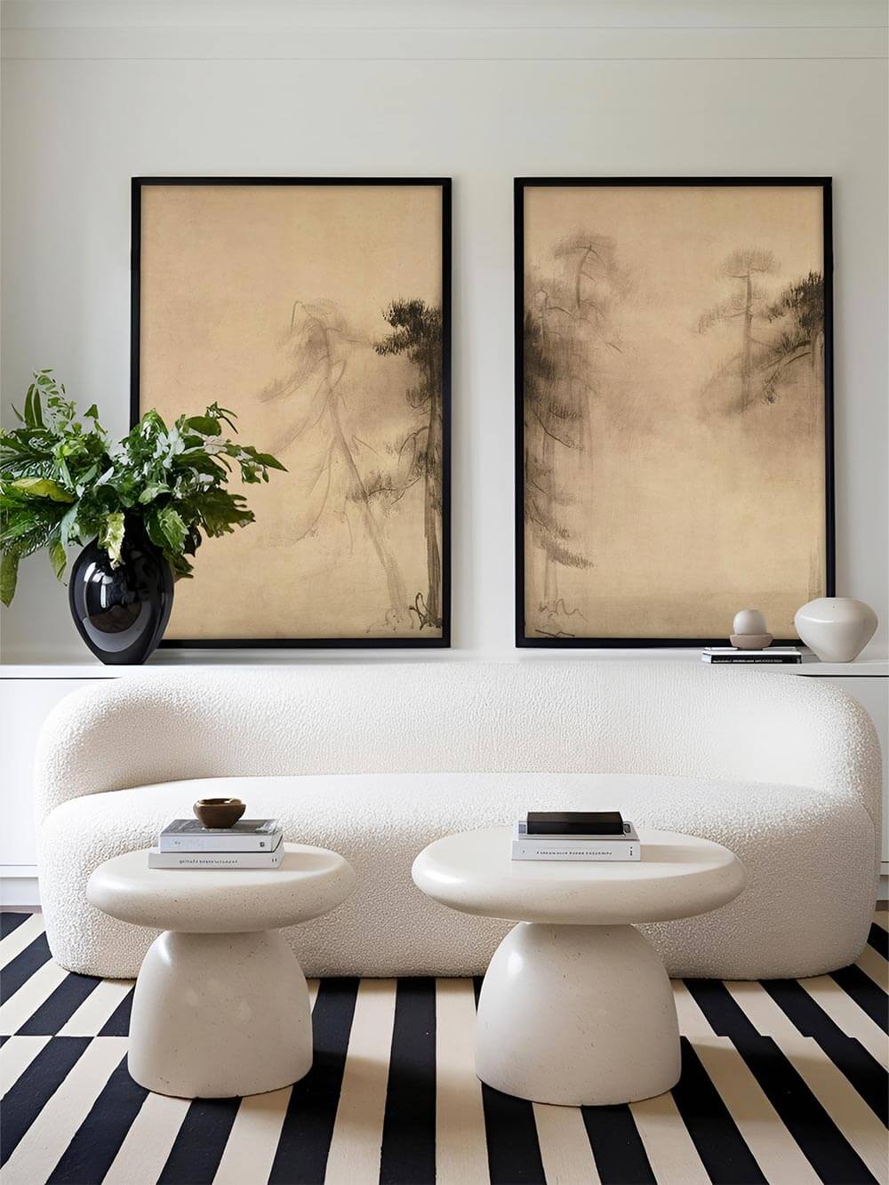 Zwei großformatige Wabi-Sabi-Kunstdrucke mit nebliger Pinienlandschaft in schwarz gerahmten Bilderrahmen. Die ruhigen Beigetöne harmonieren perfekt mit dem modernen Wohnzimmer, das mit einem weißen Sofa und stilvollen Deko-Elementen eingerichtet ist.