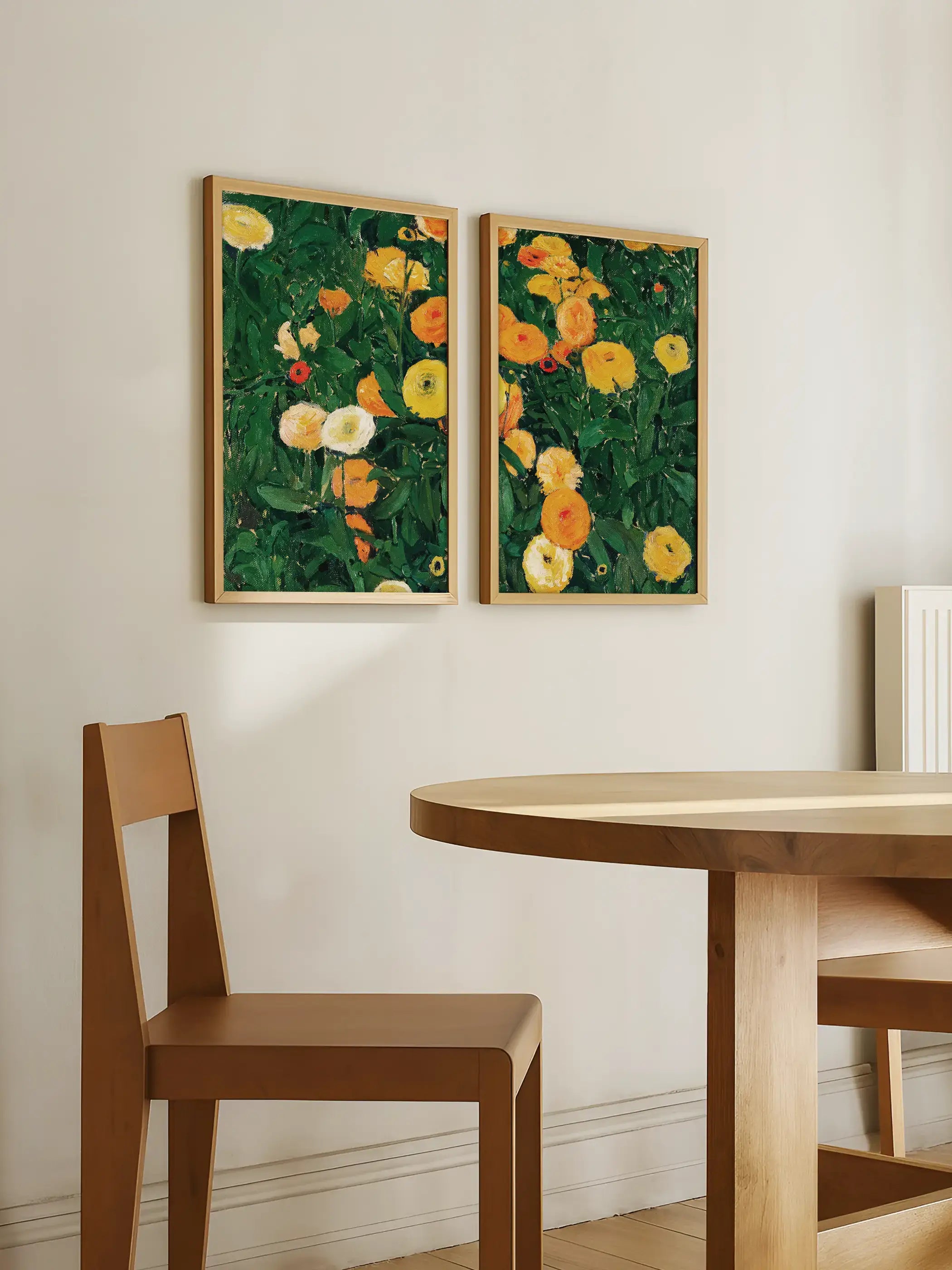 Zwei florale Kunstdrucke mit Ringelblumen hängen über einem hellen Holztisch in einem minimalistischen Esszimmer. Die grünen und goldgelben Blüten setzen frische Akzente und passen als botanische Galerie-Wand zu natürlichem Interior.
