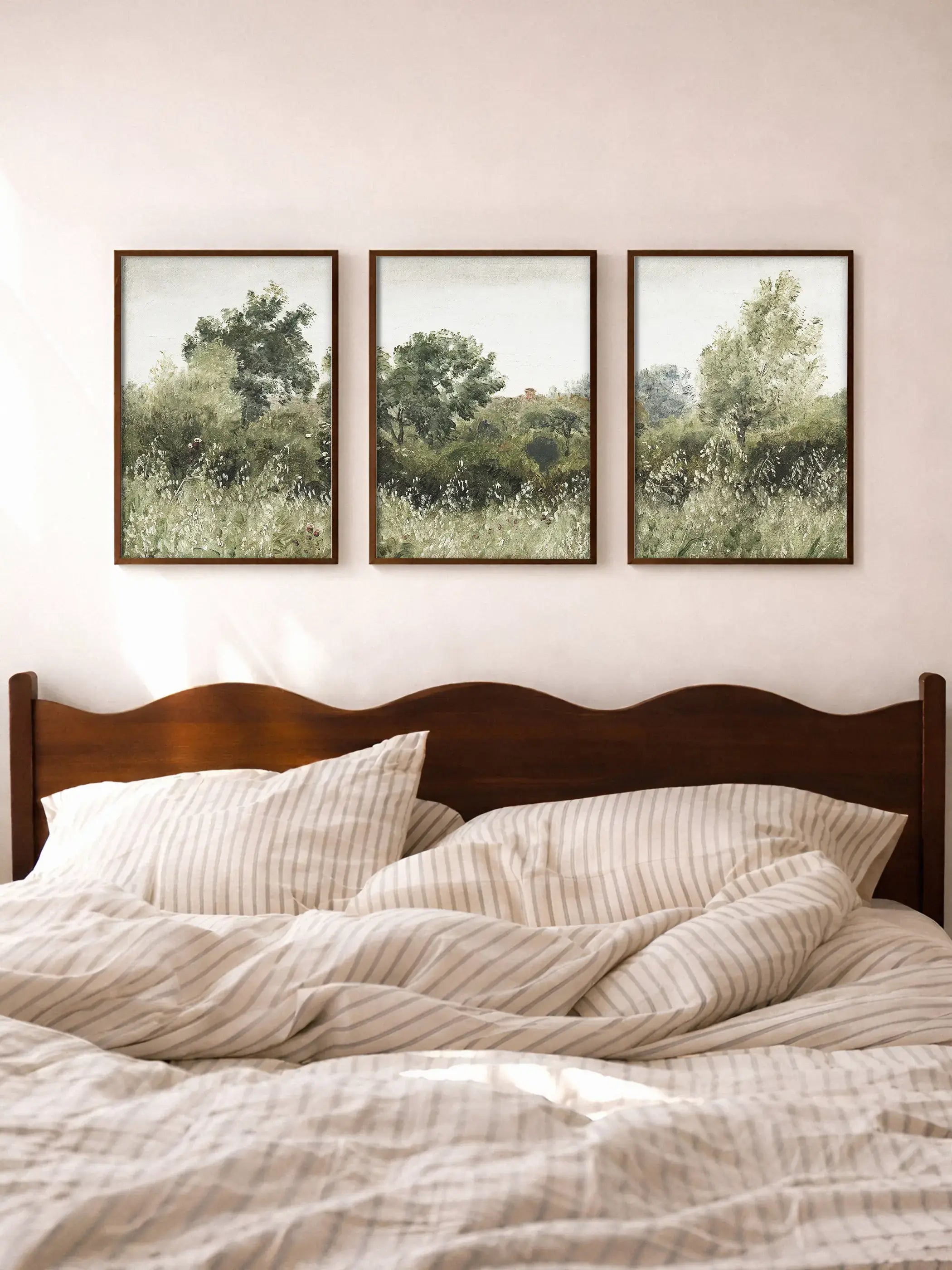 Dreiteiliges Landschafts-Wandbild mit Wiesen, Sträuchern und Bäumen in gedeckten Grünnuancen hängt über einem Bett mit neutraler Bettwäsche. Die sanfte Naturdarstellung bringt Ruhe und Leichtigkeit in ein minimalistisches Schlafzimmer.