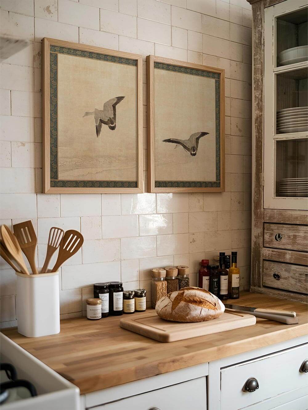 Zwei Vintage-Kunstdrucke mit fliegenden Gänsen hängen über einer Küchenzeile mit Holzarbeitsplatte. Die japanisch inspirierten Illustrationen bringen eine ruhige, wabi-sabi Atmosphäre in den Raum.