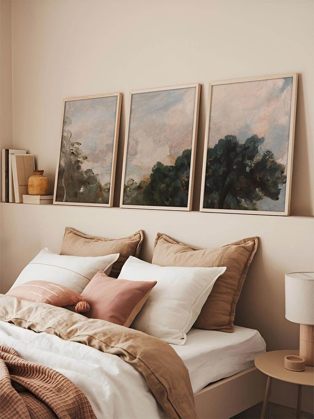 Dreiteiliges Landschafts-Kunstdruck-Set über einem Bett mit heller Bettwäsche und warmen Naturtextilien. Die abstrakten Baum- und Himmelsmotive in sanften Grün-, Grau- und Beigetönen schaffen eine ruhige, harmonische Stimmung für ein modernes Schlafzimmer.