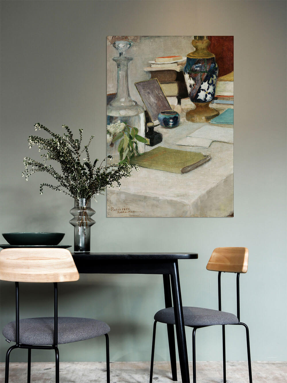 Vintage-Stillleben-Kunstdruck in einem modernen Esszimmer mit einem schwarzen Tisch und minimalistischen Holzstühlen. Der Kunstdruck hängt an einer grünen Wand und ergänzt die dezente Dekoration mit einer Vase und einem grünen Teller auf dem Tisch. Das Zusammenspiel von Farben schafft eine ruhige und stilvolle Atmosphäre.