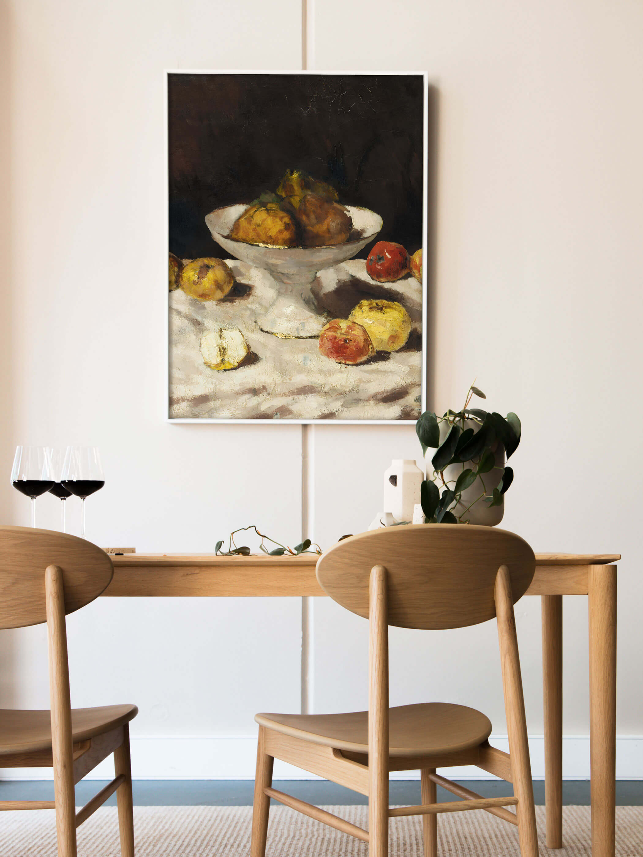 Gerahmter Kunstdruck mit Äpfeln und Birnen hängt über einem Holztisch mit Rotweingläsern und einer grünen Pflanze. Das warme Stillleben Wandbild setzt einen erdigen Akzent im hellen, skandinavisch anmutenden Esszimmer.