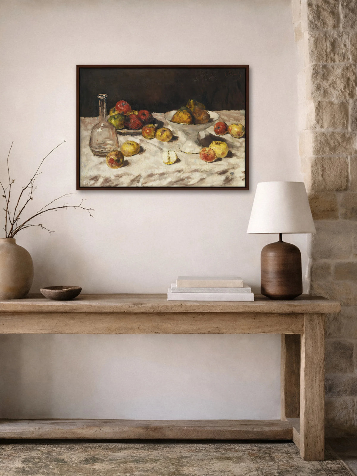 Leinwandbild mit Äpfeln und Karaffe im braunen Rahmen im Flur über einer alten Holzkonsole mit Tonvase, Holzschale, Büchern und Tischlampe neben Natursteinwand