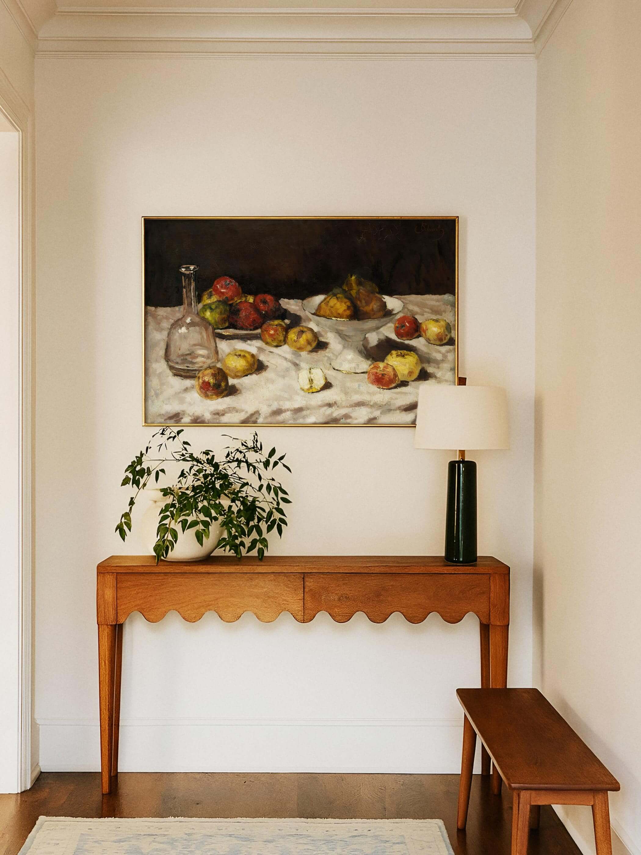 Golden gerahmter Kunstdruck mit Stillleben-Motiv hängt über einer Holzkonsole mit Pflanze und grüner Tischlampe im hellen Flur. Der warme Bildton harmoniert mit dem naturbelassenen Holz und der ruhigen Raumgestaltung.