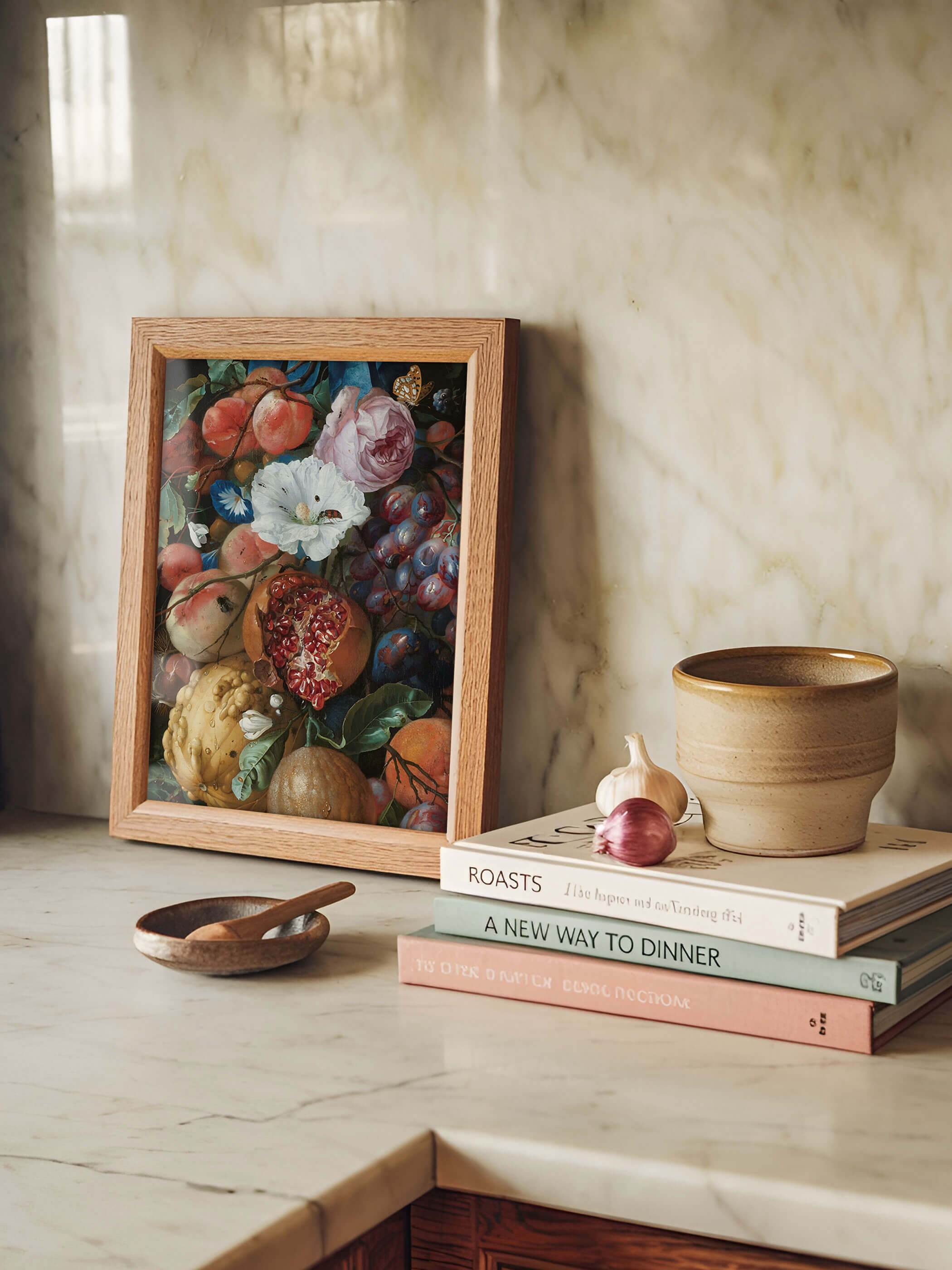 Gerahmter Kunstdruck mit barocker Früchtegirlande aus Pfirsichen, Granatapfel und Trauben lehnt auf einer Marmorarbeitsplatte neben Kochbüchern und einer Keramikschale. Der Holzrahmen und die kräftigen Farben setzen einen dekorativen Akzent in der hellen Küche.