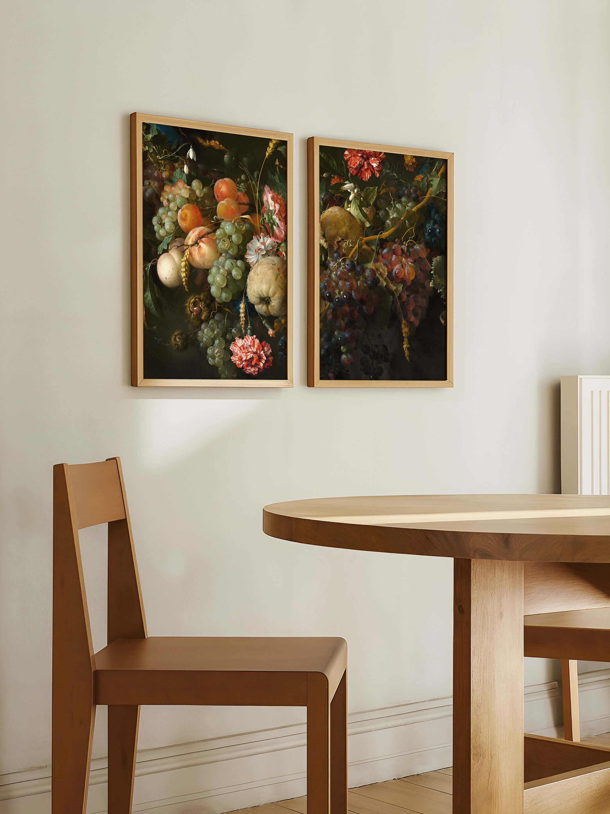 Zwei hell gerahmte Kunstdrucke mit barocken Fruchtgirlanden aus Trauben, Pfirsichen und dunklen Weintrauben hängen nebeneinander über einem runden Holztisch. Das Diptychon aus hellem und dunklem Stillleben setzt einen stimmungsvollen Akzent im Esszimmer.
