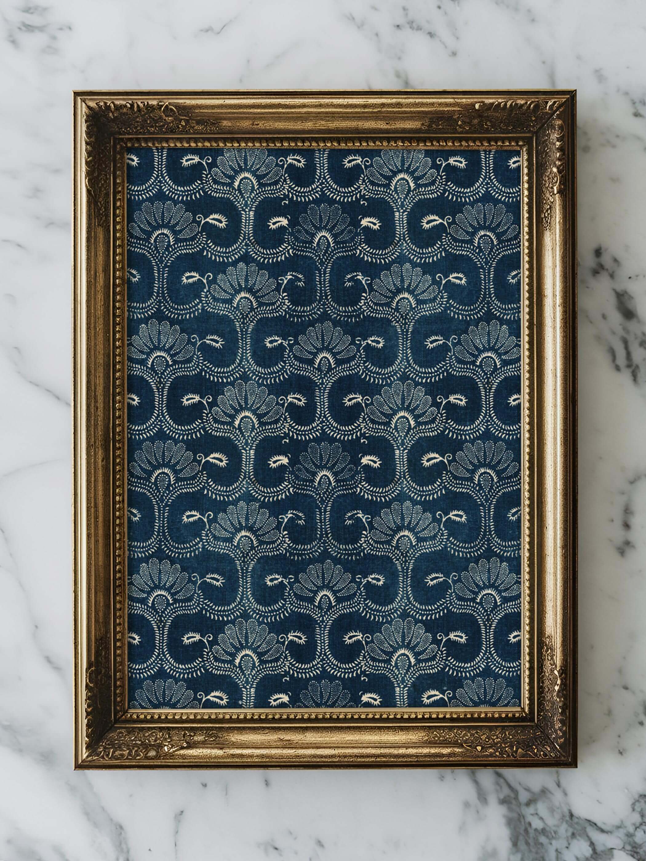 Nahaufnahme eines Vintage-Stoff-Kunstdrucks mit blauen und weißen floralen Mustern in einem goldverzierten Rahmen, auf einer Marmoroberfläche platziert.