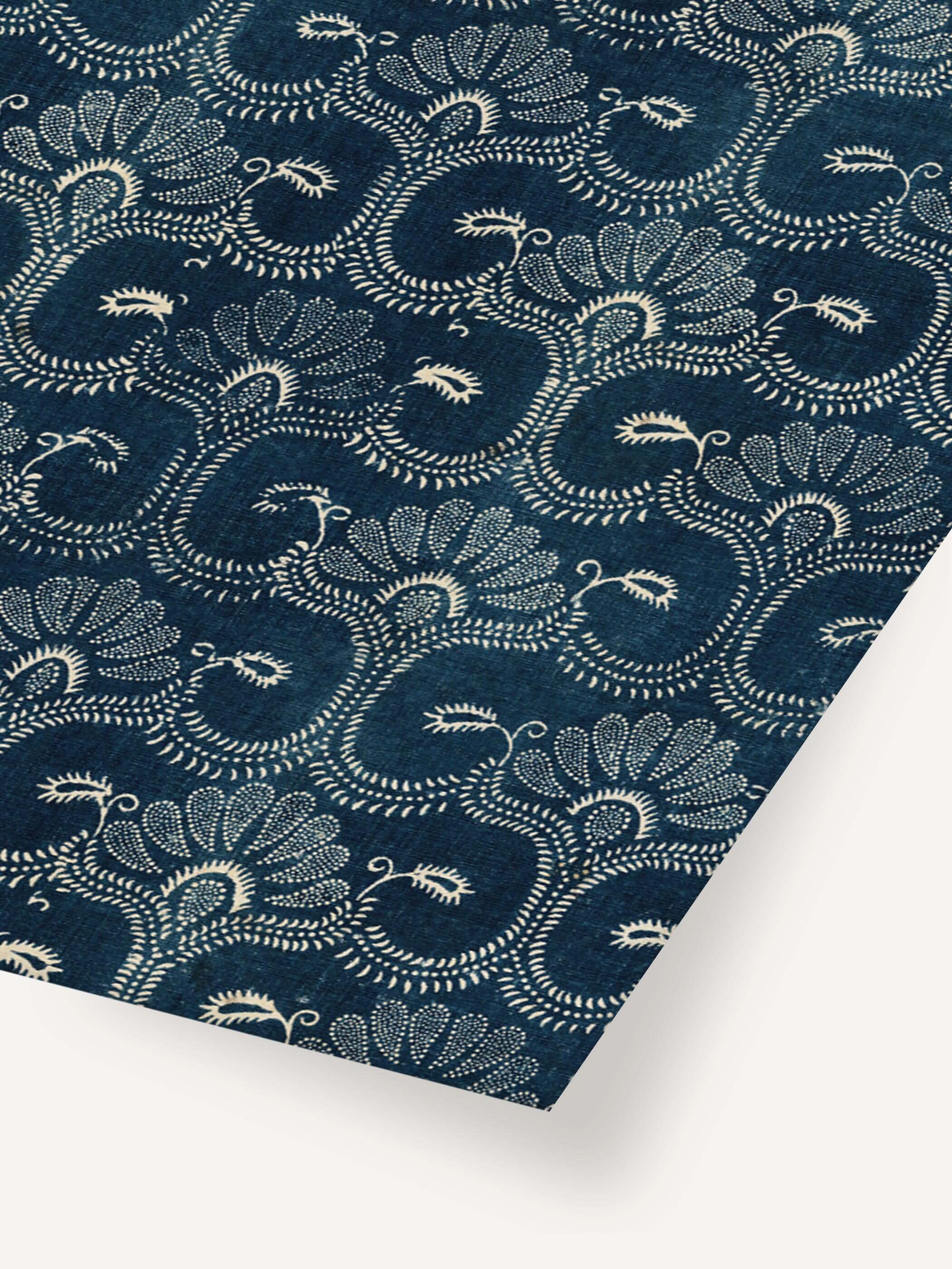 Nahaufnahme eines Kunstdrucks mit Vintage-Stoffmuster in Blau mit weißen floralen Verzierungen und geschwungenen Ornamenten, auf einer diagonalen Oberfläche präsentiert