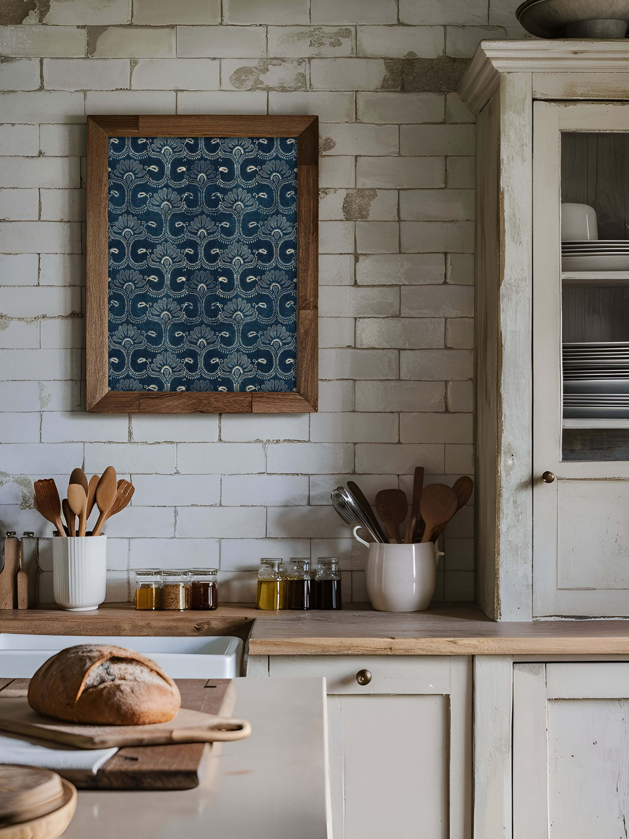 Blauer Vintage-Stoff Kunstdruck mit weißen floralen Mustern, an der Wand einer rustikalen Küche mit weißen Fliesen und hölzernen Küchenutensilien aufgehängt.