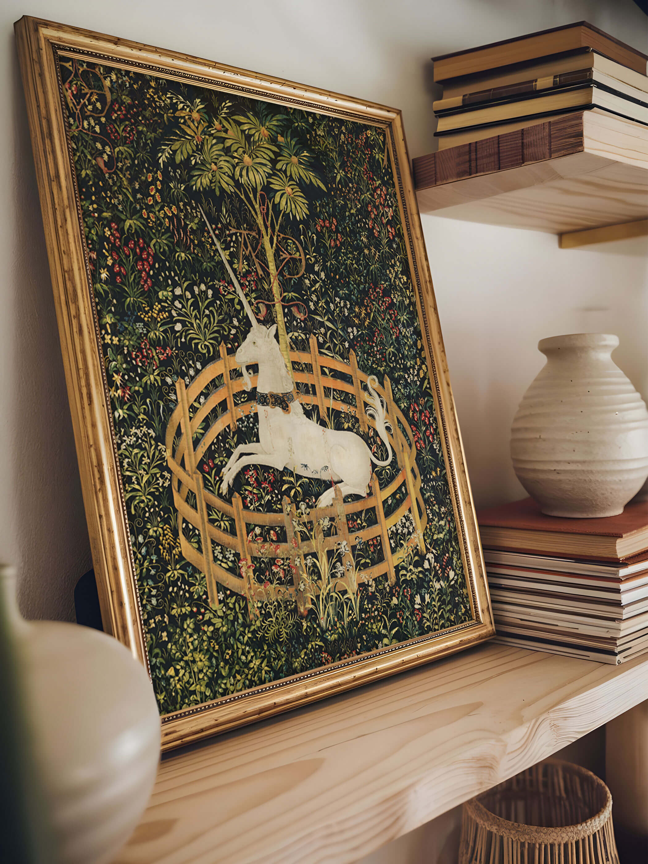 Detailansicht eines Poster des antiken Wandteppichs 'Das Einhorn ruht in einem Garten', elegant eingerahmt auf einem Bücherregal, umgeben von Keramik und Büchern.