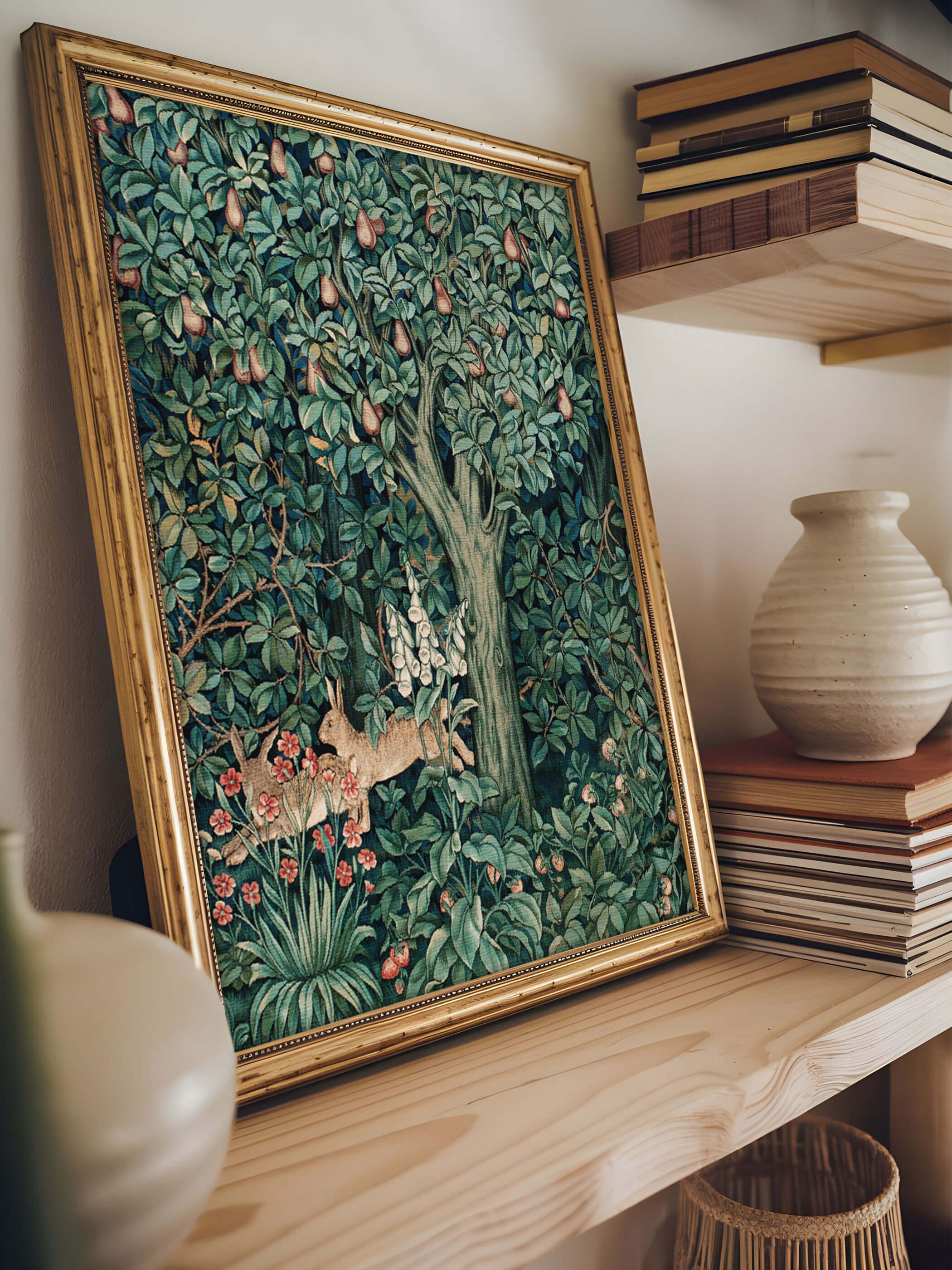 William Morris Kunstdruck in einem goldenen Rahmen, der ein detailreiches Waldmotiv mit einem Birnbaum und zwei Hasen zeigt, auf einem Regal arrangiert. Der Kunstdruck wird von Keramikobjekten und Büchern umgeben. Perfekte Dekoration für ein elegantes und naturverbundenes Interieur.