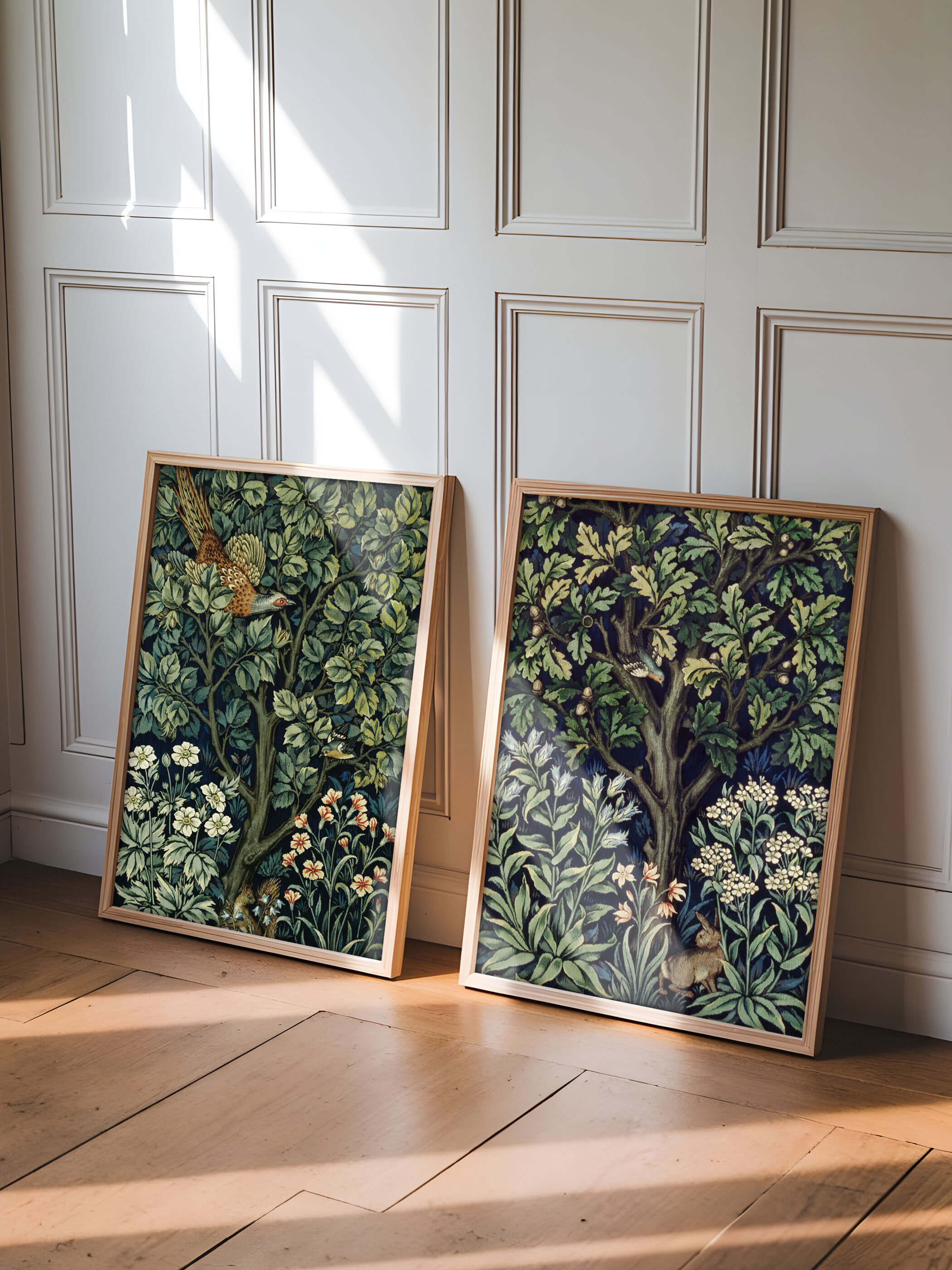 Zwei gerahmte Poster von William Morris mit Waldmotiven lehnen an einer weißen Wand. Der eine Druck zeigt einen Vogel in einem Baum, der andere ein Eichhörnchen und ein Hase zwischen Blumen und Blättern. Perfekte Deko für ein natürliches und zeitloses Ambiente.