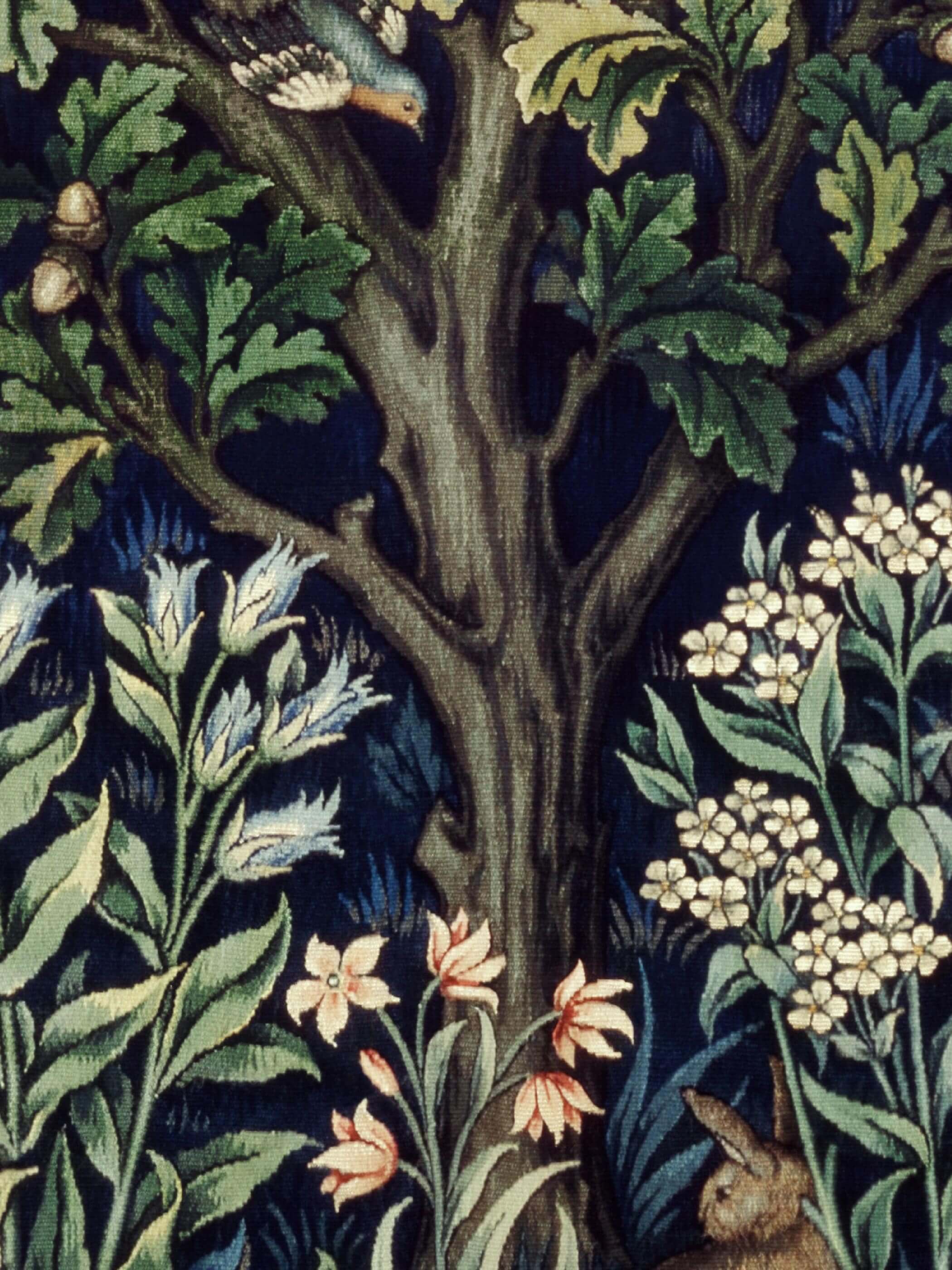 Detail eines William Morris Kunstdrucks mit einem Baumstamm, Eichenblättern, Blumen und einem Hasen. Oben sitzt ein kleiner Vogel im Geäst, umgeben von Blättern und Eicheln.