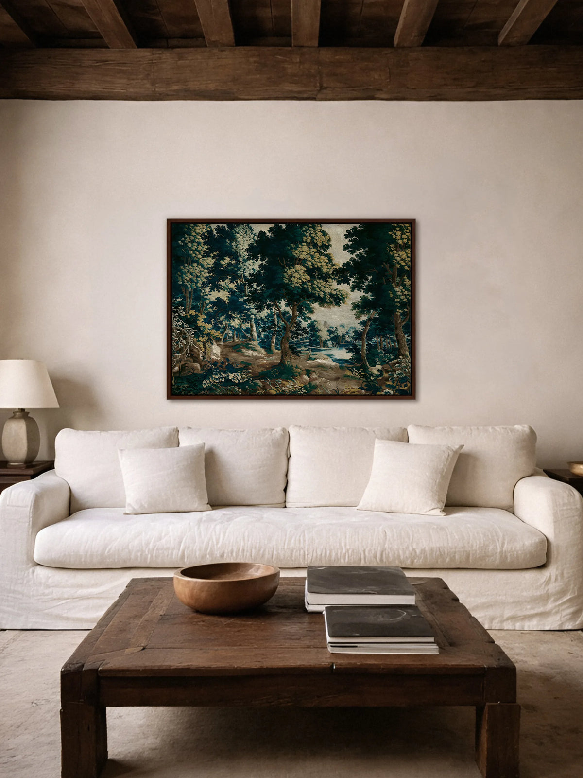 Wandteppich Motiv mit Wald als Leinwandbild im braunen Rahmen über einem weißen Leinensofa, Couchtisch aus dunklem Holz und Holzbalken an der Decke