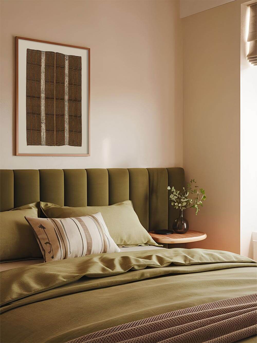 Textiler Kunstdruck mit dunklen, grafischen Mustern hängt über einem Bett mit grünen Textilien und sanftem Licht. Das Wandbild ergänzt eine warme, entspannte Atmosphäre und passt zu ruhiger Schlafzimmer-Deko und zeitloser Wohnästhetik.