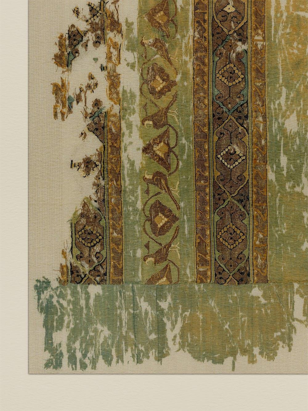 Nahaufnahme eines textilen Kunstmotivs mit vertikalen Ornamentstreifen in gedeckten Grün-, Ocker- und Brauntönen, bei dem abgenutzte Strukturen und fragmentierte Muster sichtbar werden und eine ruhige Wabi-Sabi-Ästhetik mit antiker Anmutung entsteht.