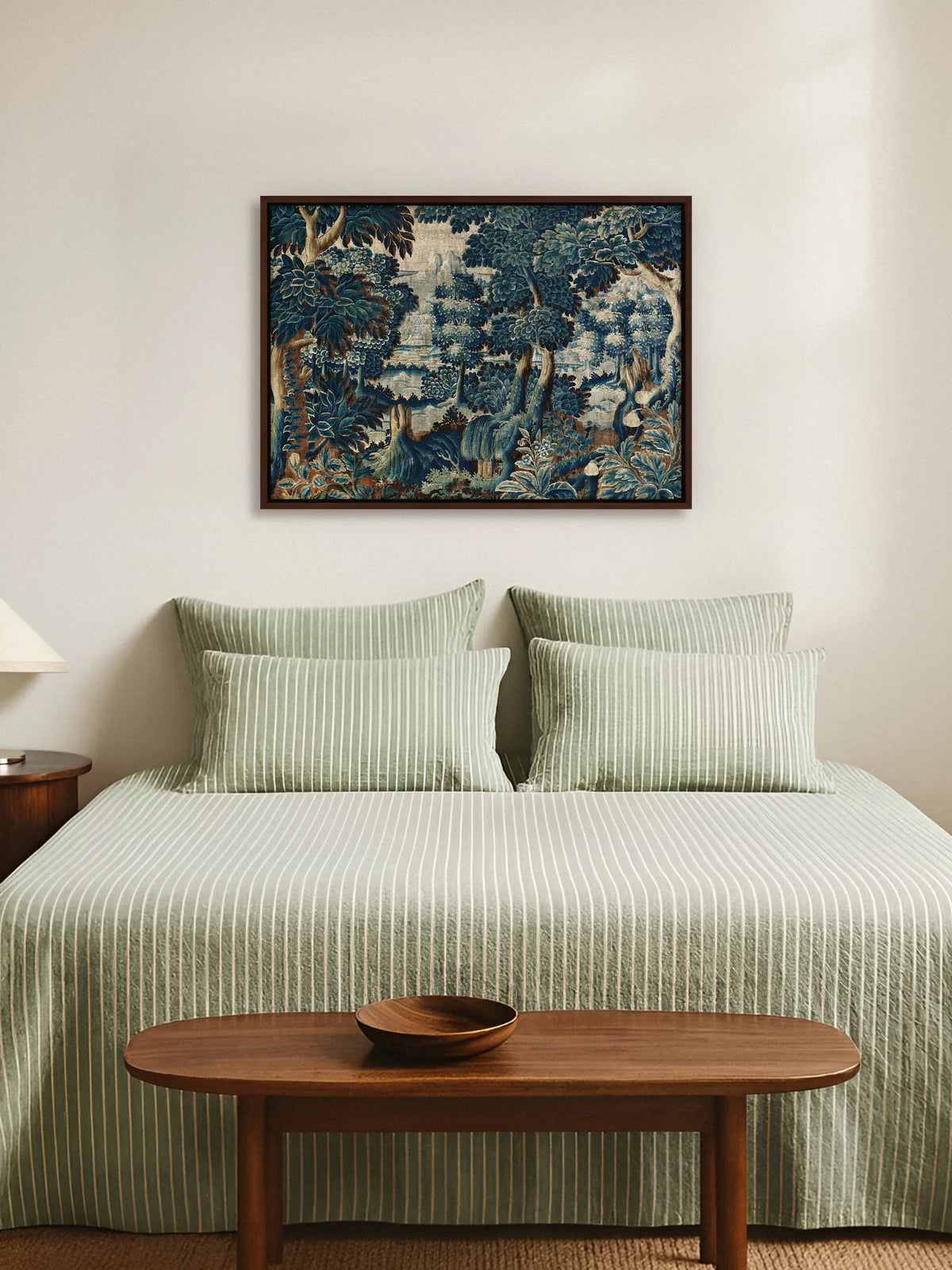 Leinwandbild mit blauer Verdure im braunen Rahmen über einem Bett mit salbeigrün gestreifter Bettwäsche und Bank aus Nussbaum